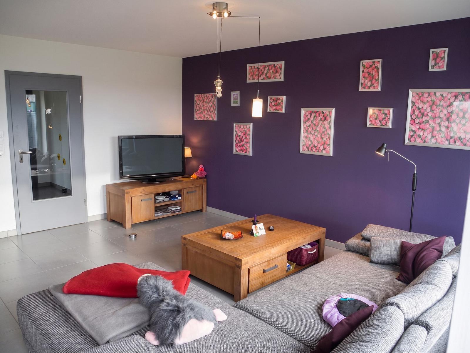 Wohnzimmer mit lila Wand, Sofa, Couchtisch und Fernseher.