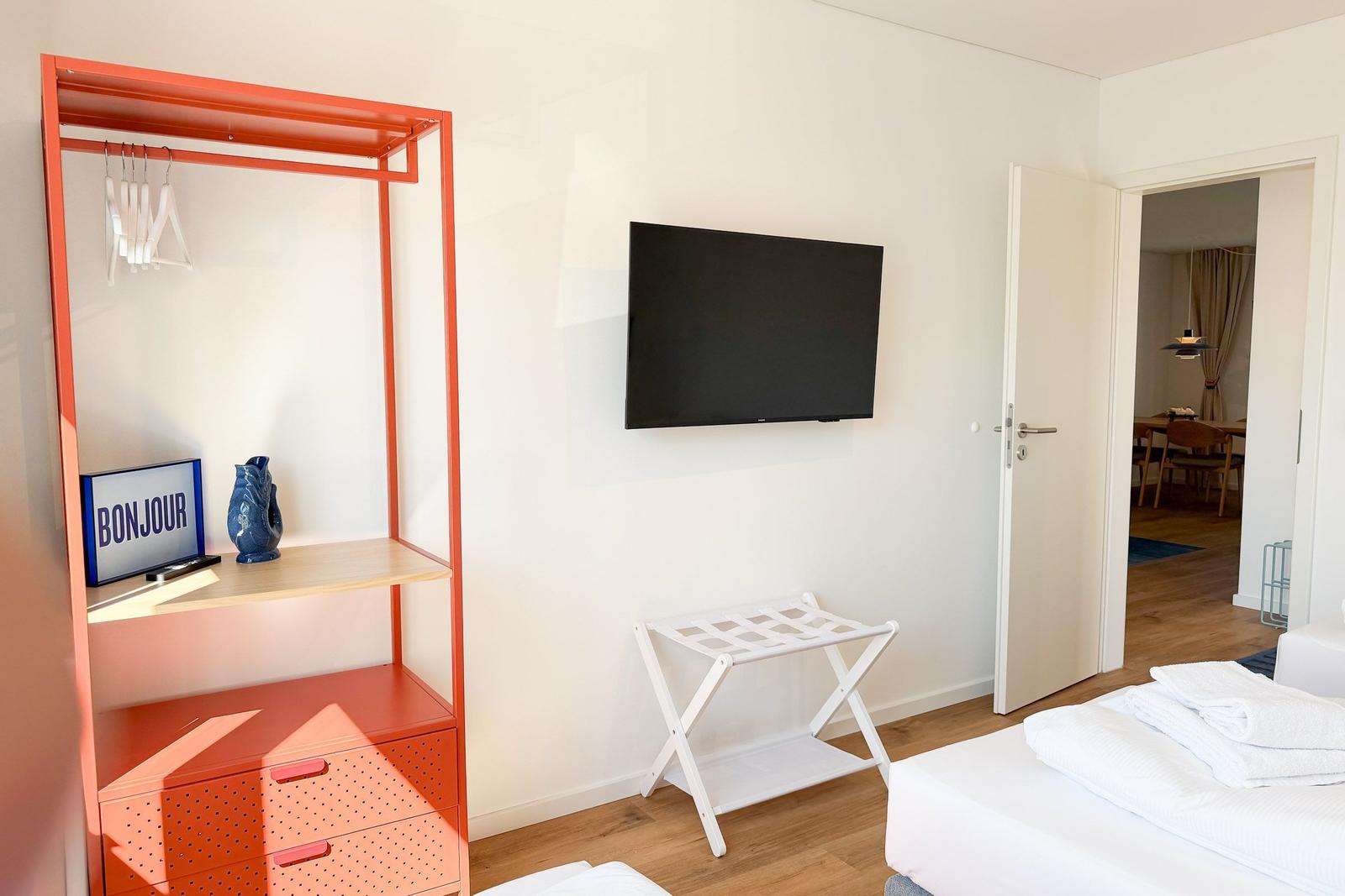Schlafzimmer mit Bett, Kleiderschrank und Fernseher. Tür führt in Wohnbereich.