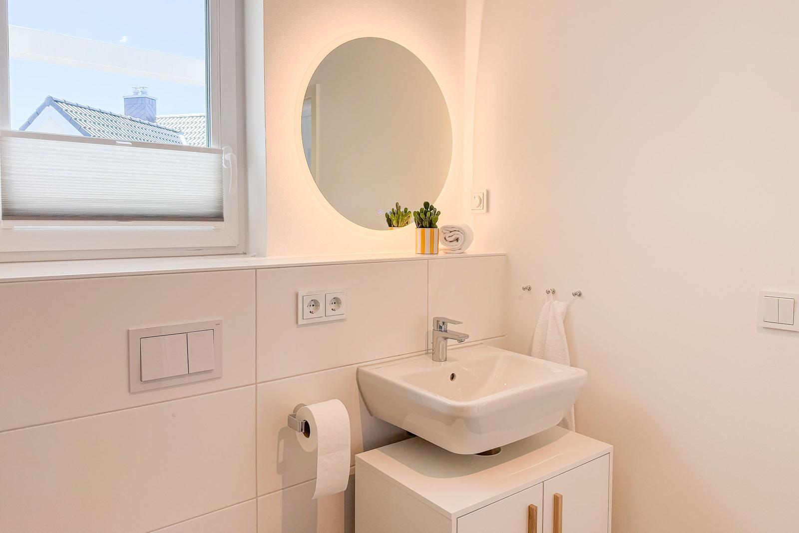 Badezimmer mit Waschbecken, Spiegel und Fenster.