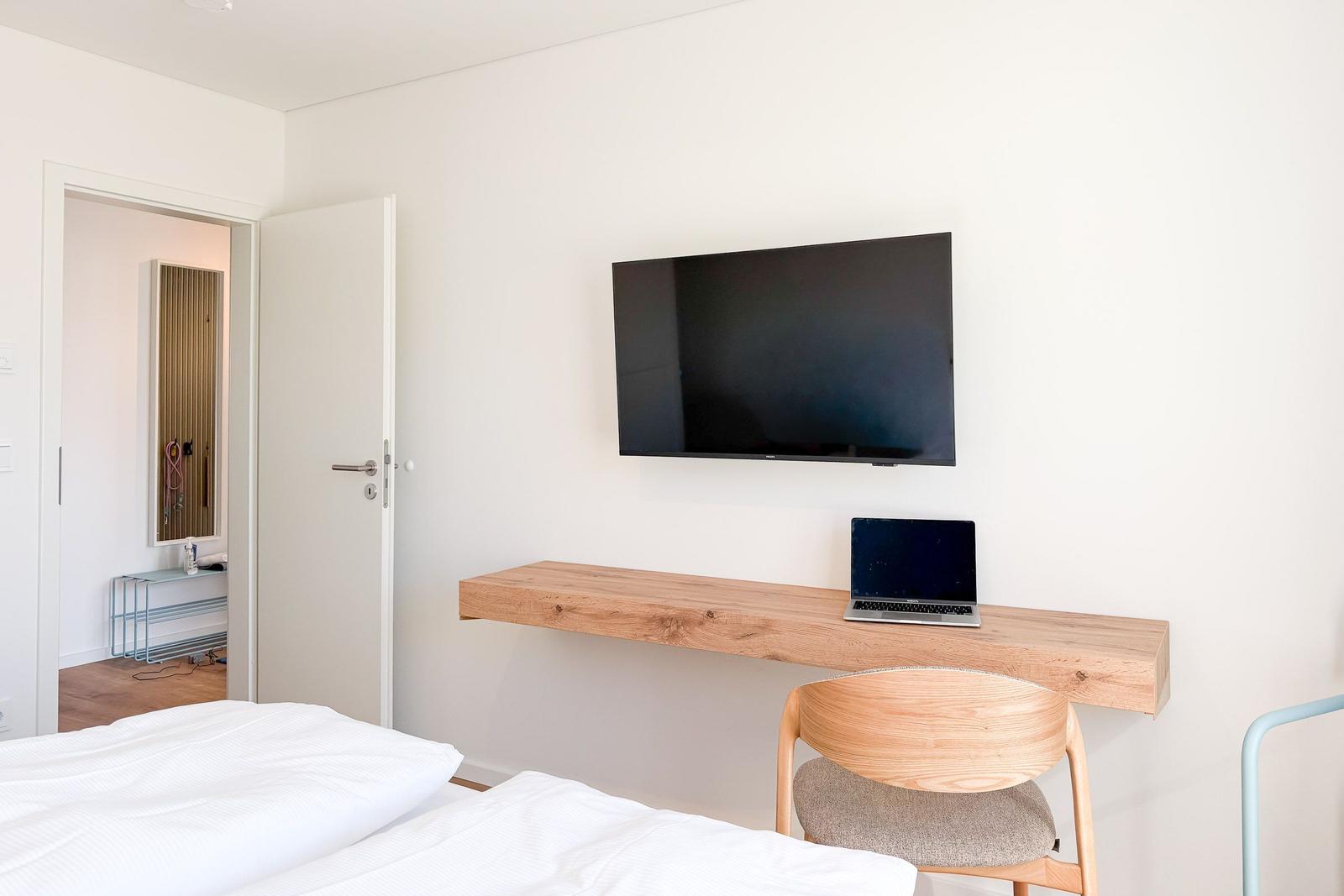 Schlafzimmer mit Bett, Schreibtisch und Fernseher an der Wand