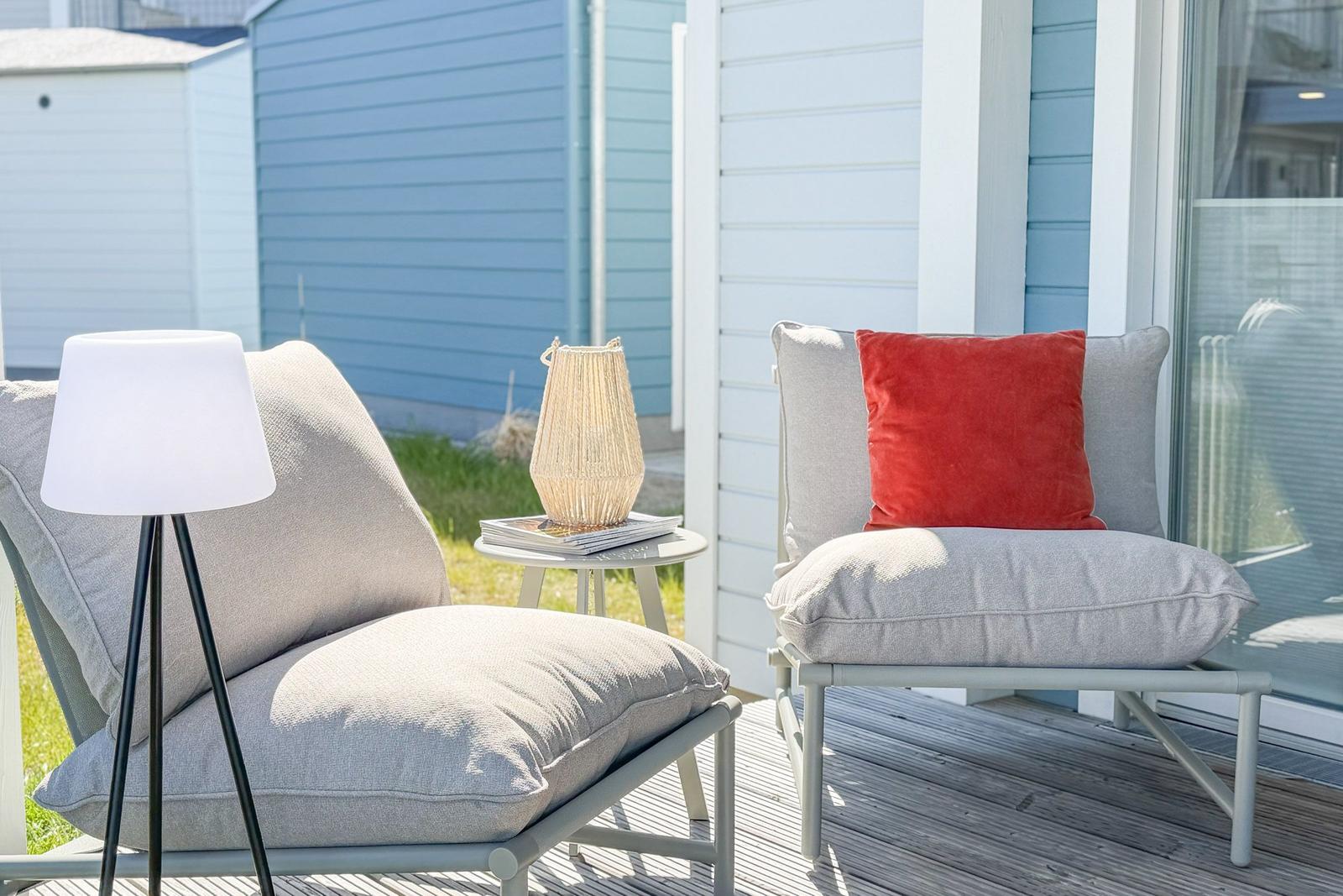 Terrasse mit zwei Sesseln, einem Tisch und einer Stehlampe. Hintergrund: blaue Hauswand.
