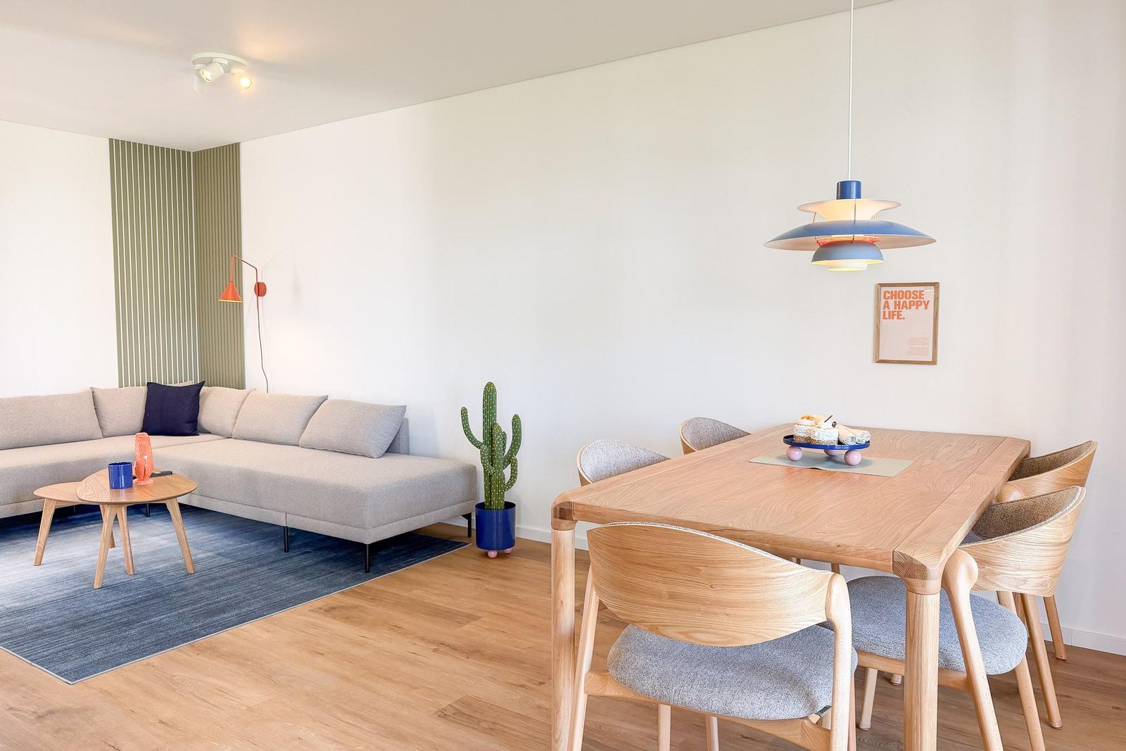 Wohn- und Essbereich mit Sofa, Tisch und Stühlen. Wandlampe und Pflanze sind sichtbar.