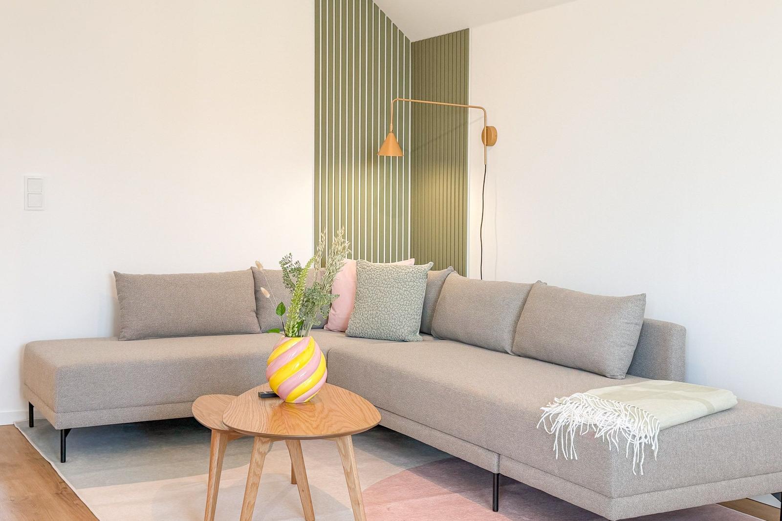 Ein Wohnzimmer mit einem grauen Sofa, einem Holztisch und einer Wand mit grünen Streifen.
