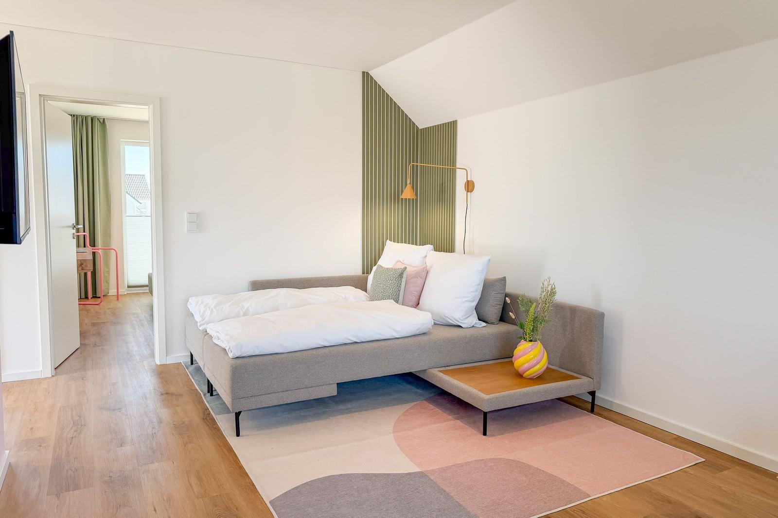 Schlafzimmer mit Bett, Teppich und Wandbeleuchtung. Tür führt zu einem Balkon.