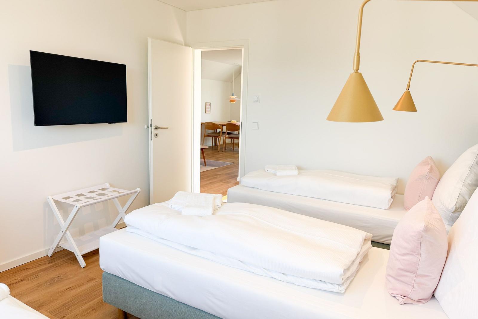 Zwei Betten mit weißen Laken, goldene Deckenleuchten und Fernseher an der Wand.