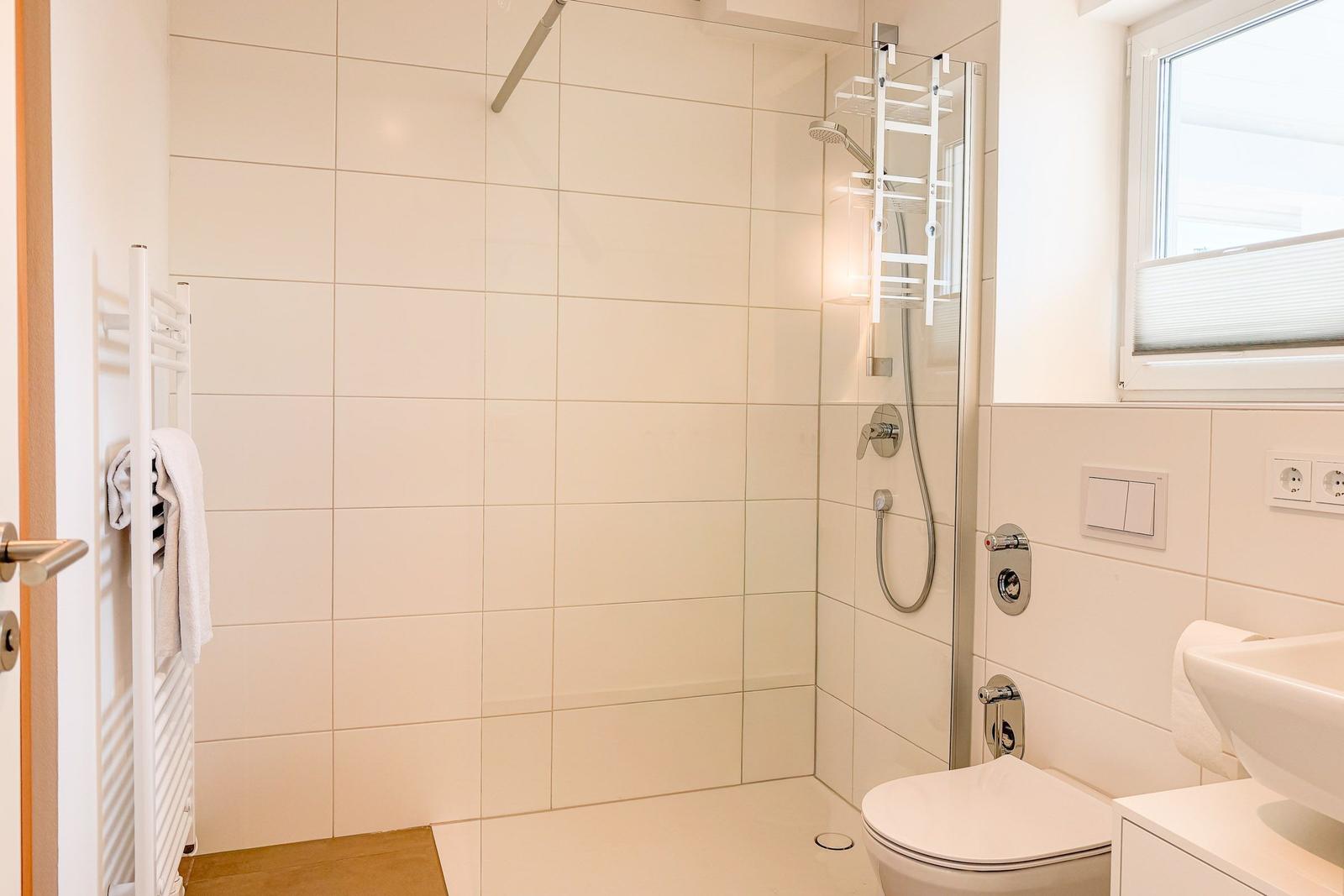 Badezimmer mit Dusche, Toilette und Waschbecken. Fenster mit Jalousie.