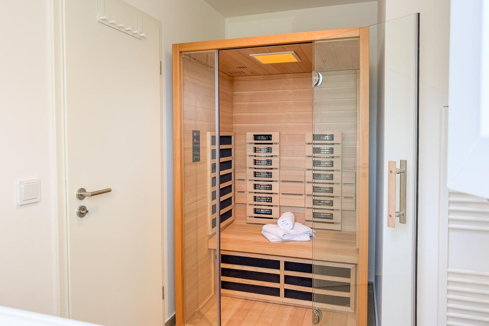 Eine Sauna mit Holzwand, Sitzbank und Handtuch. Die Tür ist offen.