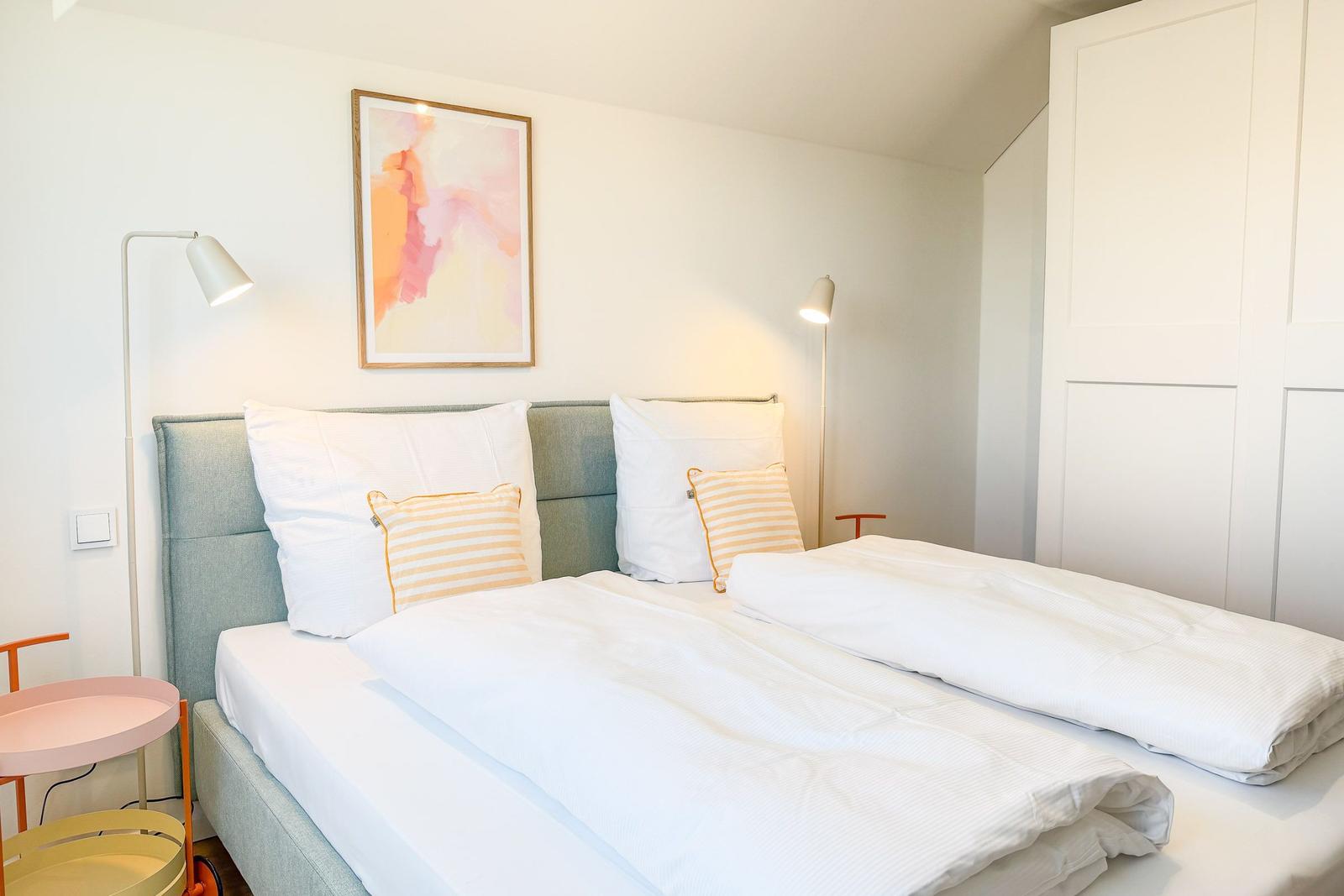 Schlafzimmer mit Doppelbett, zwei Stehlampen und einem Bild an der Wand.