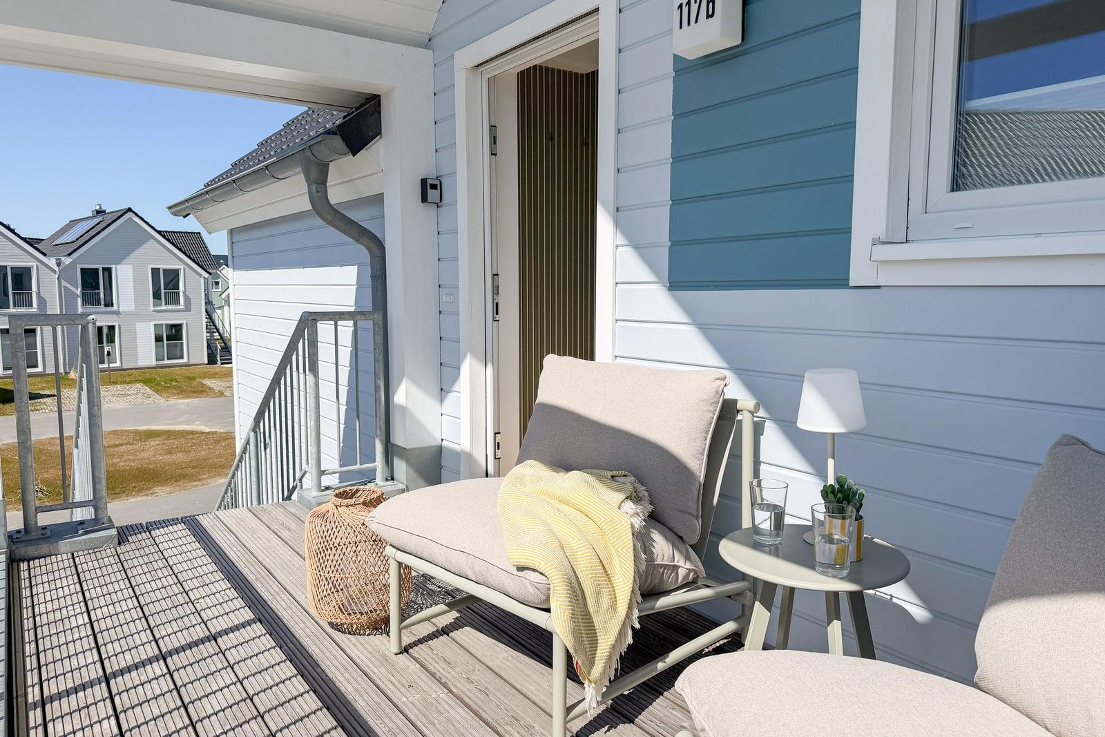 Terrasse mit Liege, Tisch und Pflanzen. Hintergrund: Haus mit Balkon und Garten.