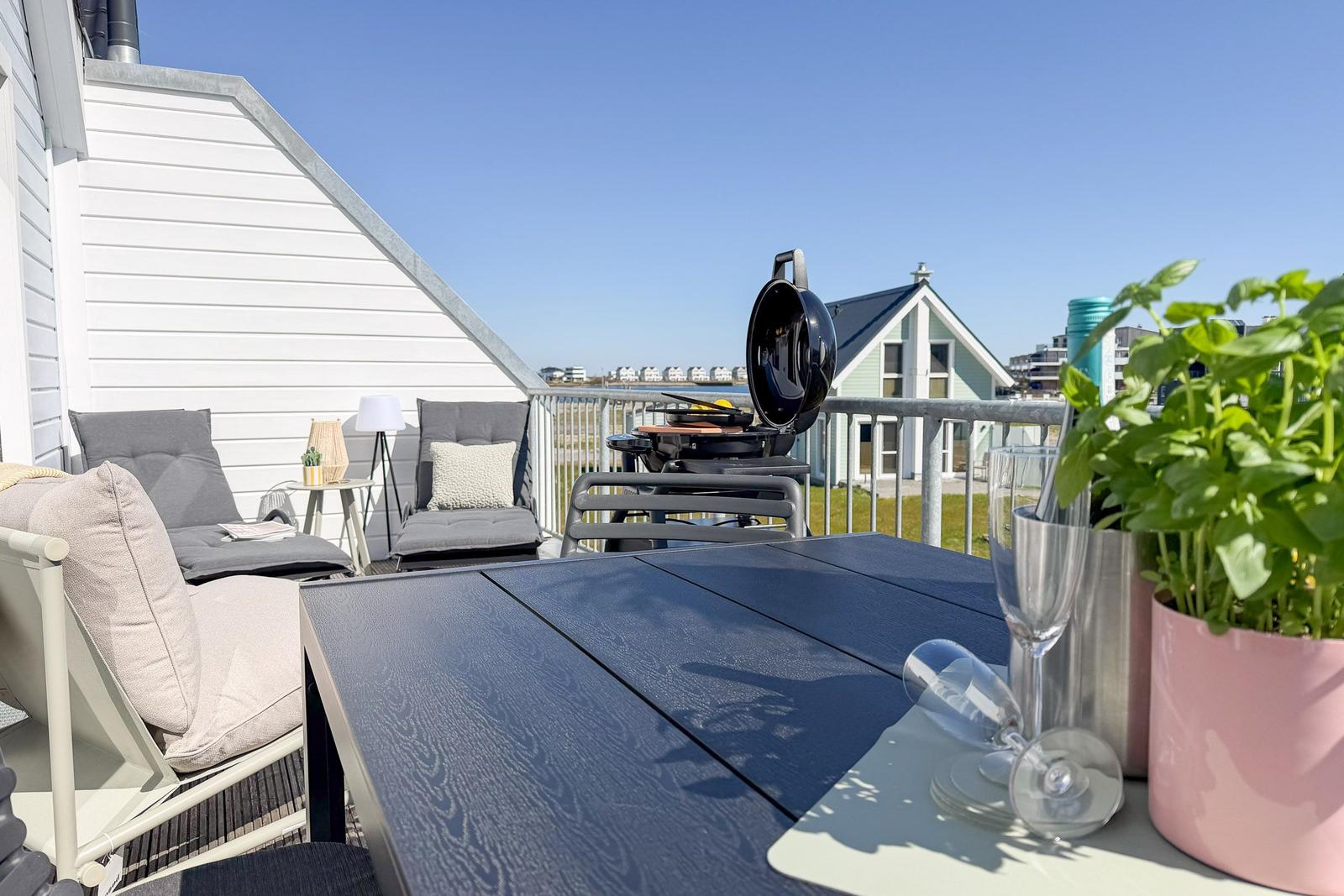 Terrasse mit Tisch, Stühlen, Grill und Pflanze. Blick auf Haus und Grünfläche.