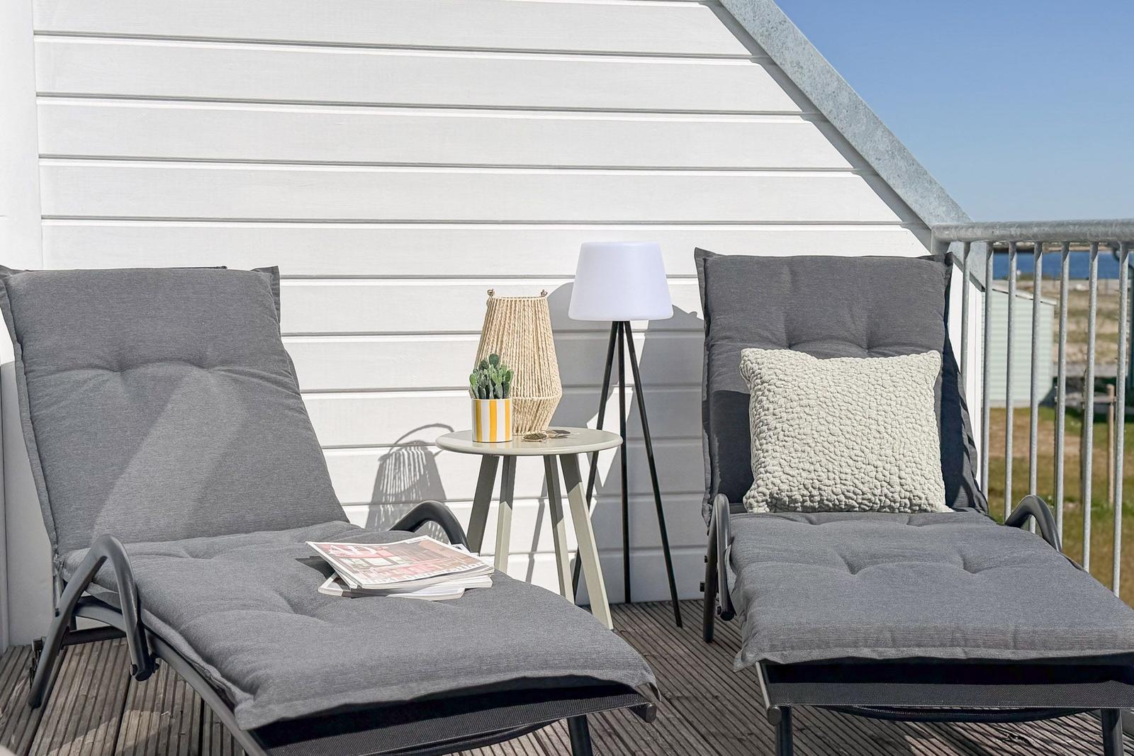 Zwei Liegestühle mit Kissen stehen auf einer Terrasse vor einer weißen Wand.