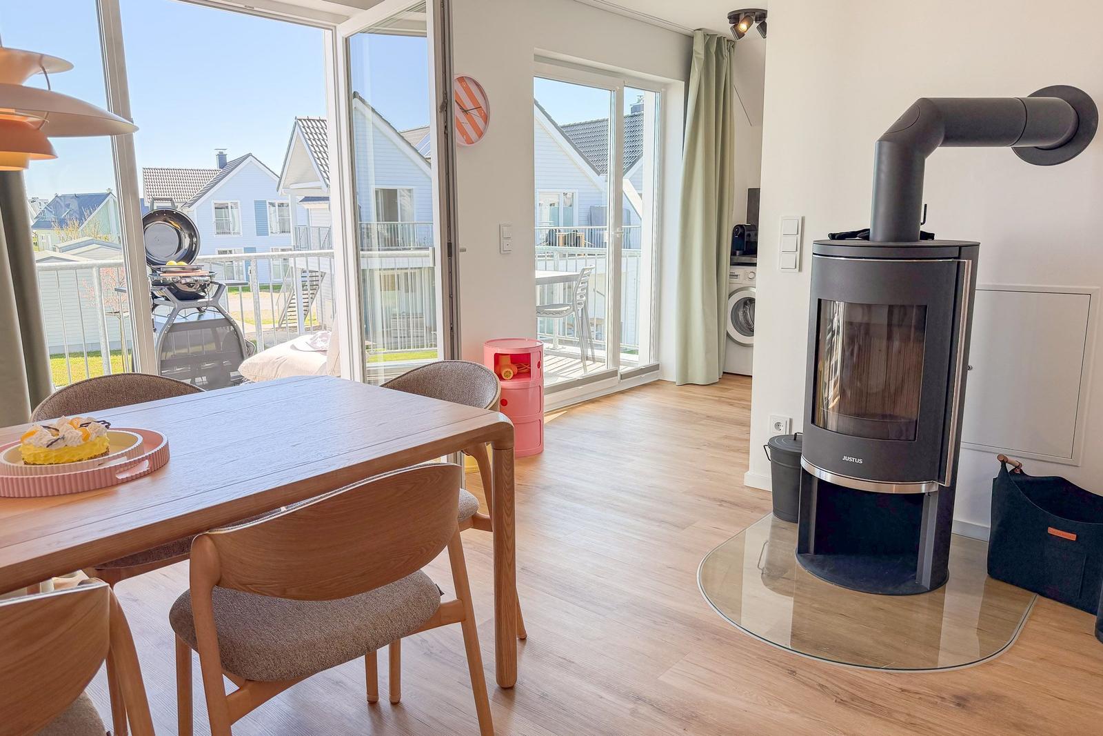Esszimmer mit Holztisch, Stühlen und Kaminofen. Durchgang zur Terrasse mit Blick auf Nachbarhäuser.