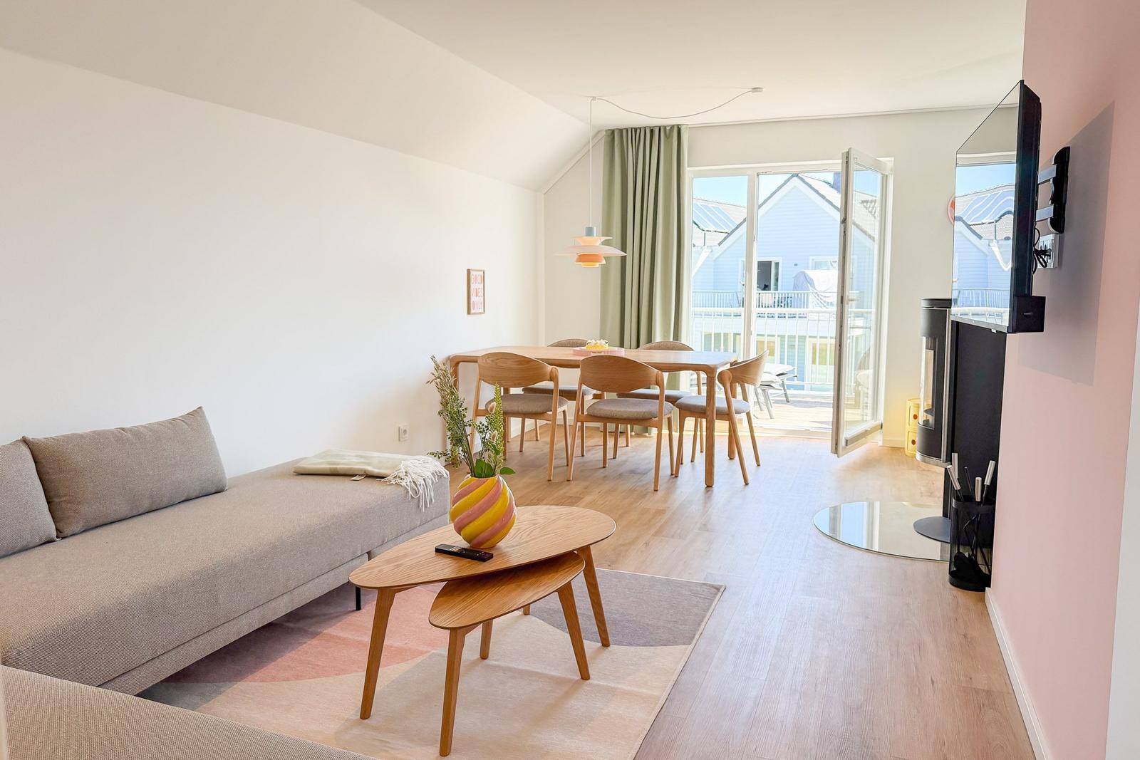 Wohn- und Essbereich mit Sofa, Tisch, Stühlen und TV. Durchgang zur Terrasse mit Blick auf Haus.