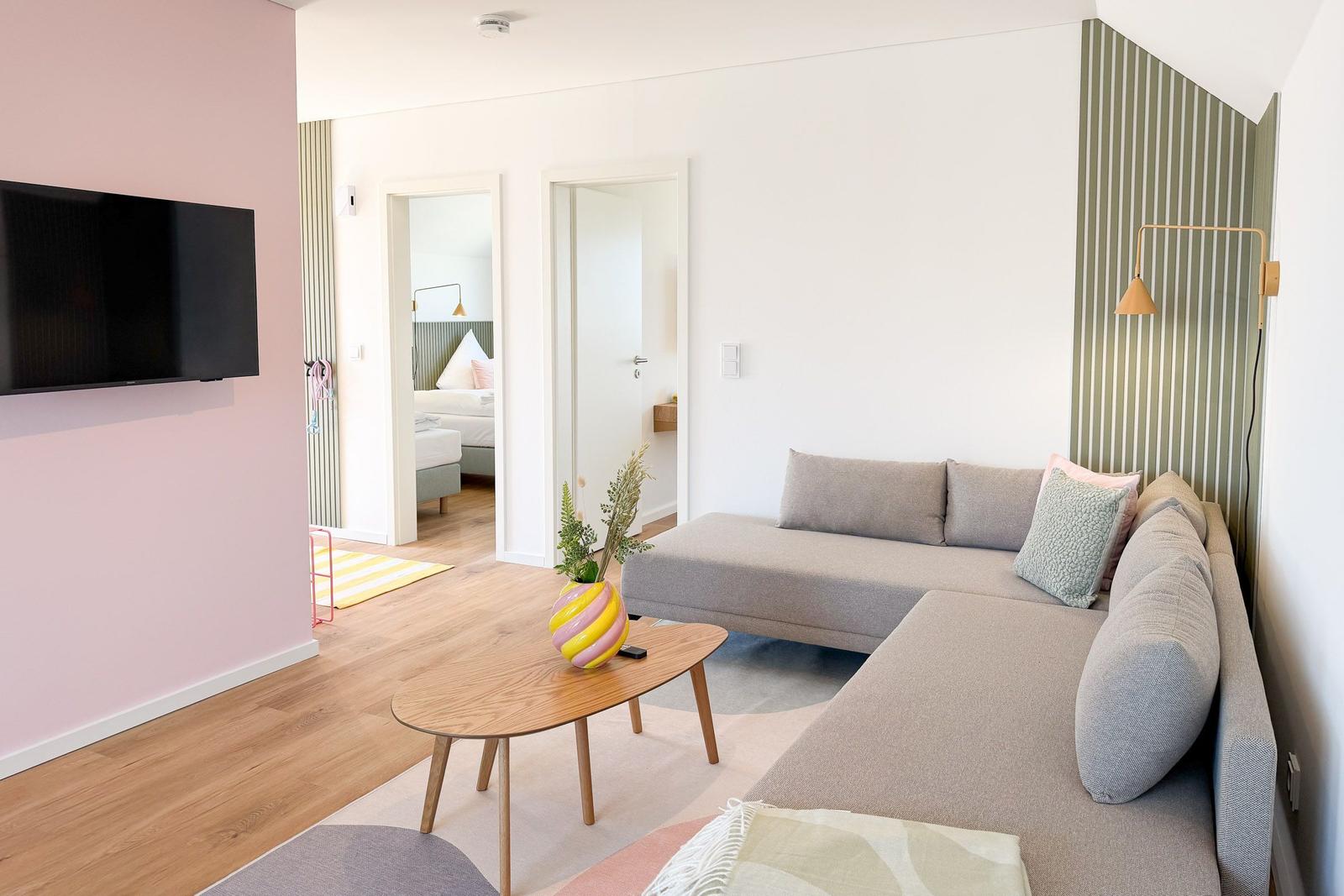 Wohnzimmer mit Sofa, Couchtisch und Fernseher. Blick in Schlafzimmer und Bad.