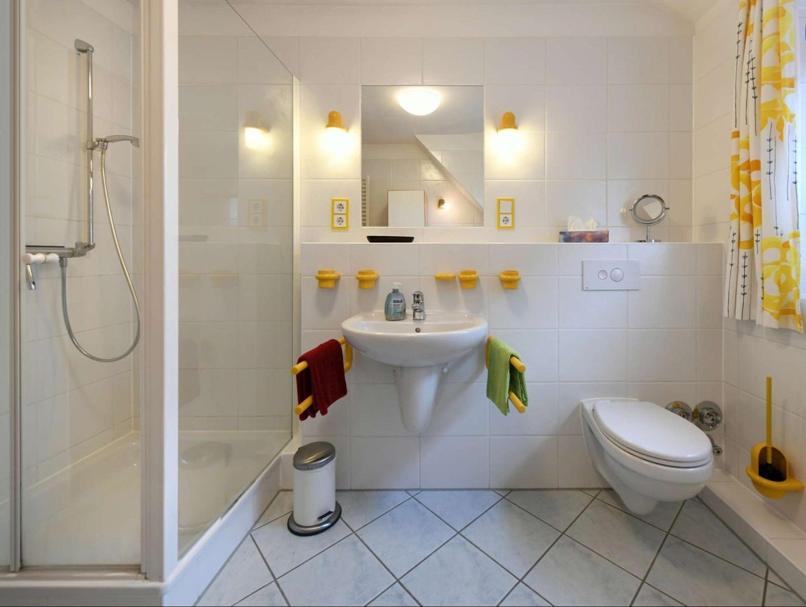 Badezimmer mit Dusche, Waschbecken und Toilette. Gelbe Halterungen und ein gelb-weißes Badetuch.