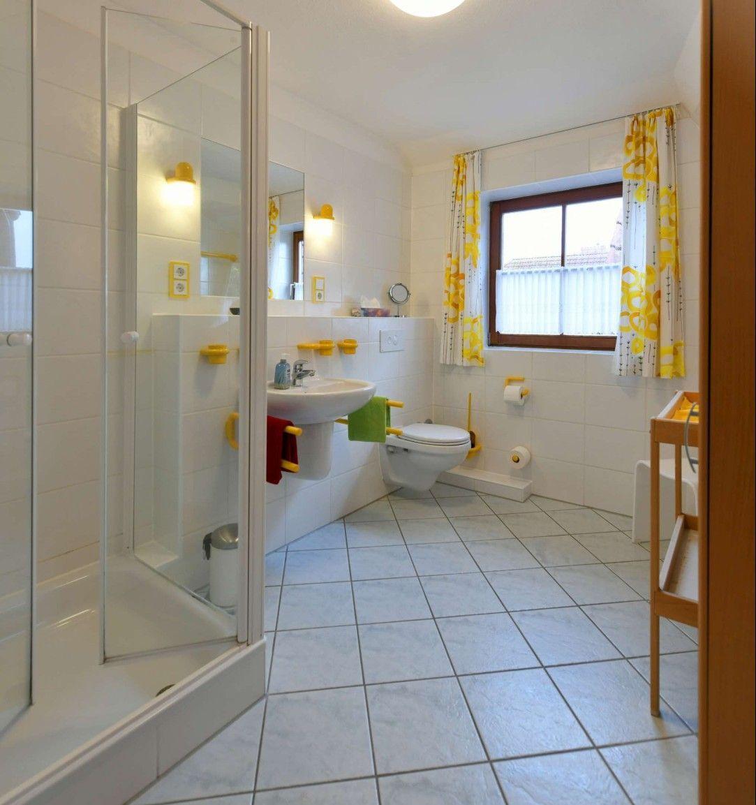 Badezimmer mit Dusche, Waschbecken und Toilette. Fenster mit gelben Vorhängen.