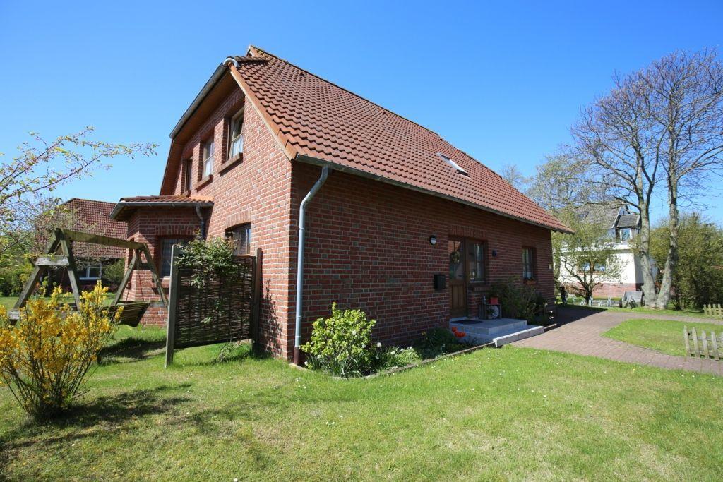 Rotes Backsteingebäude mit Garten und Spielgeräten. Helle Fenster und Terrasse.