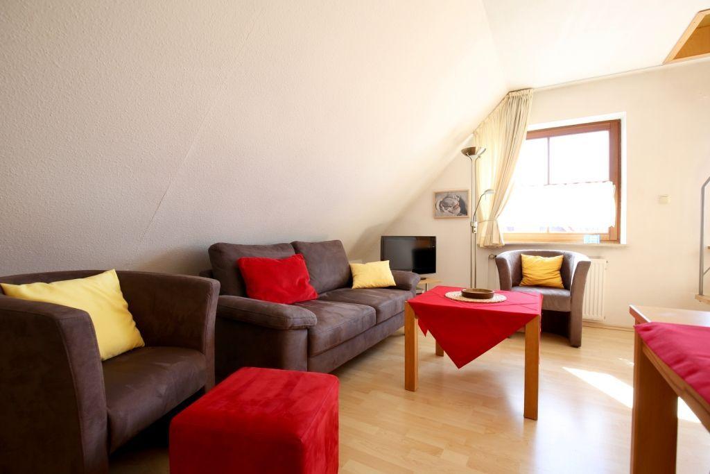 Wohnzimmer mit Sofa, Sessel und Tisch unter Dachschrägen.