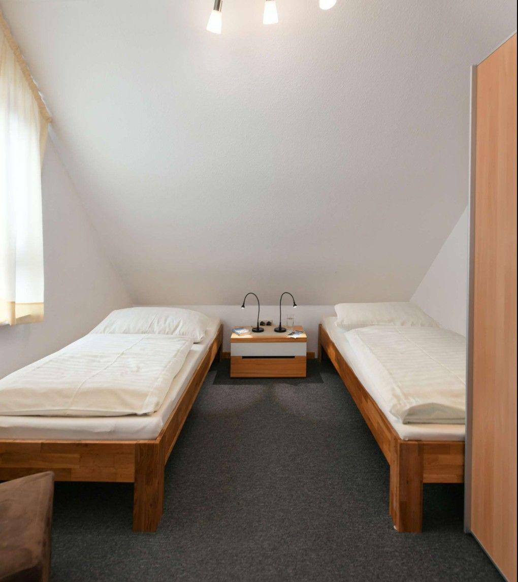 Zwei Einzelbetten mit Nachttisch und Lampen in einem Dachzimmer mit Fenster und Kleiderschrank.