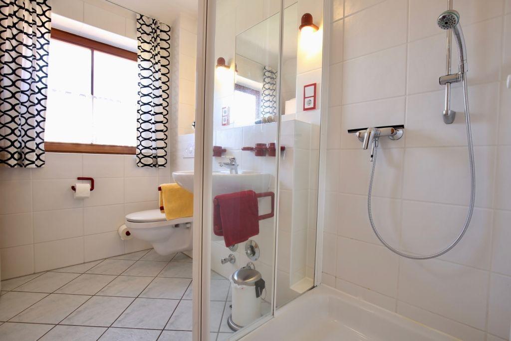 Badezimmer mit Dusche, Toilette und Waschbecken. Fenster mit Vorhängen.