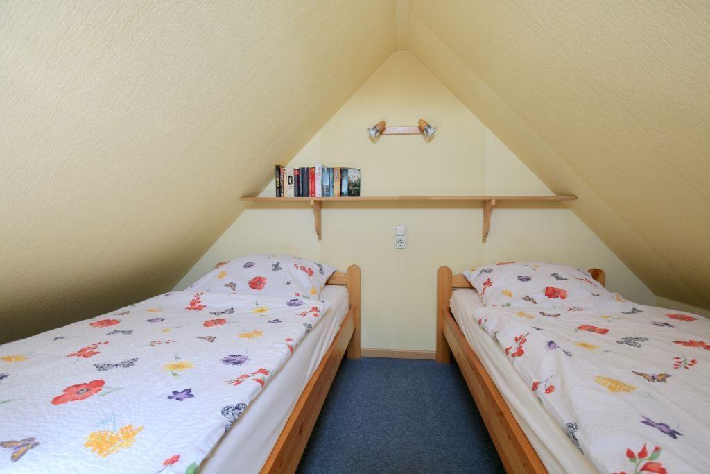 Zwei Einzelbetten unter Dachschräge mit Bücherregal und Deckenbeleuchtung.