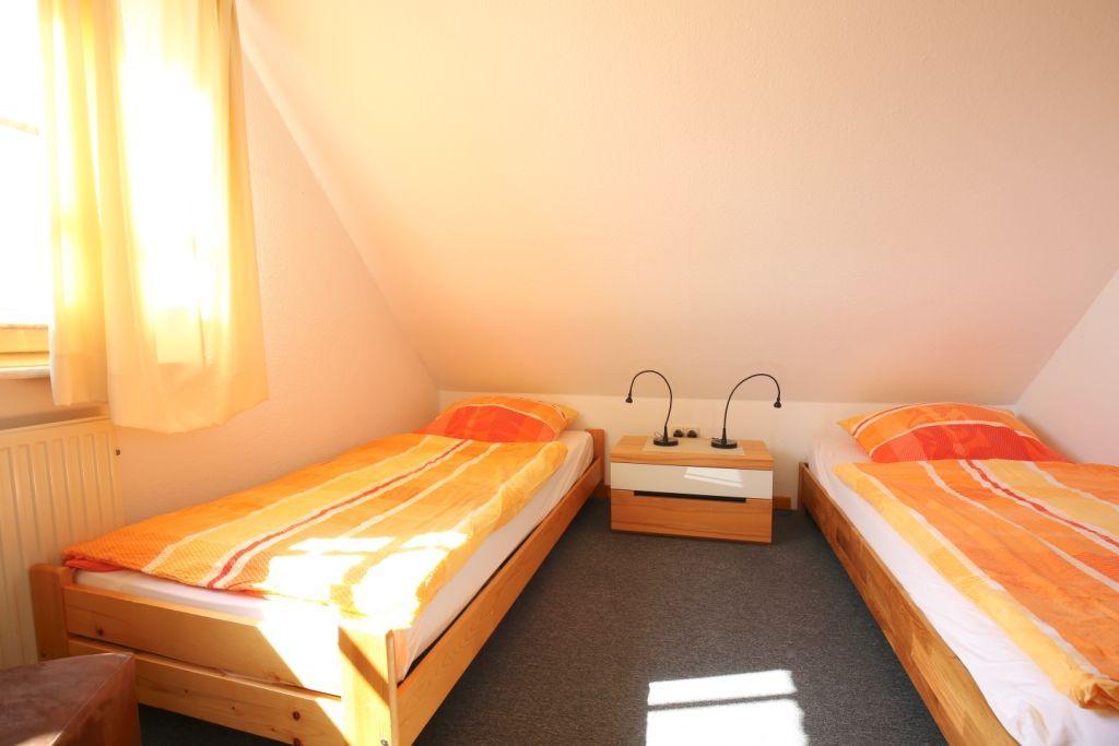 Zwei Einzelbetten mit orangefarbenen Bettwäschen und einem Nachttisch mit zwei Lampen.