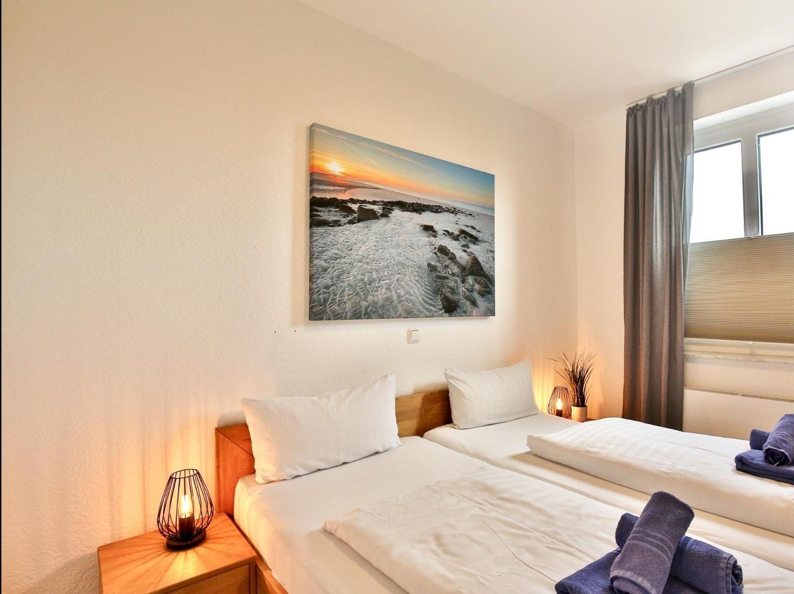 Zwei Betten mit weißen Laken, Wandbild und Fenster mit Vorhängen.