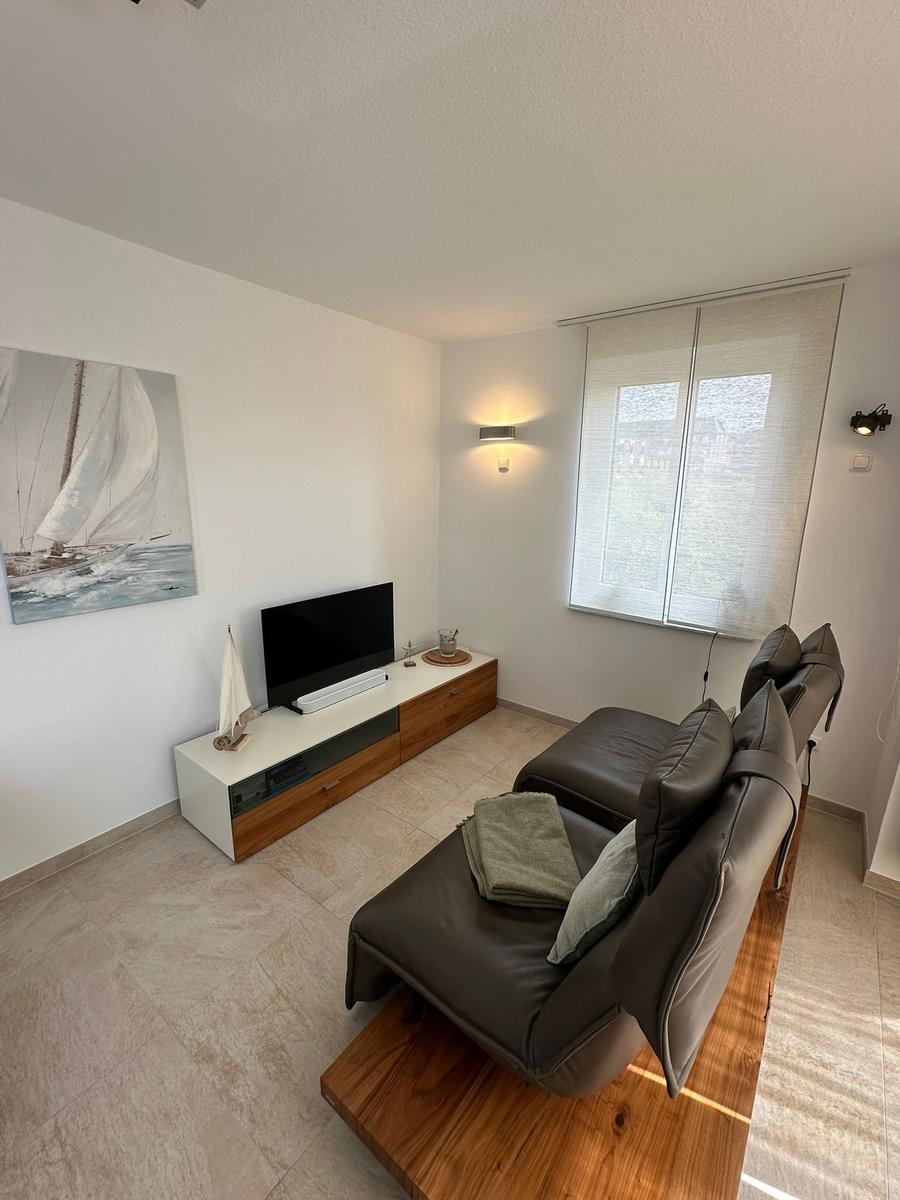 Wohnzimmer mit Ledersofa, Fernseher und Wandbild mit Segelboot.