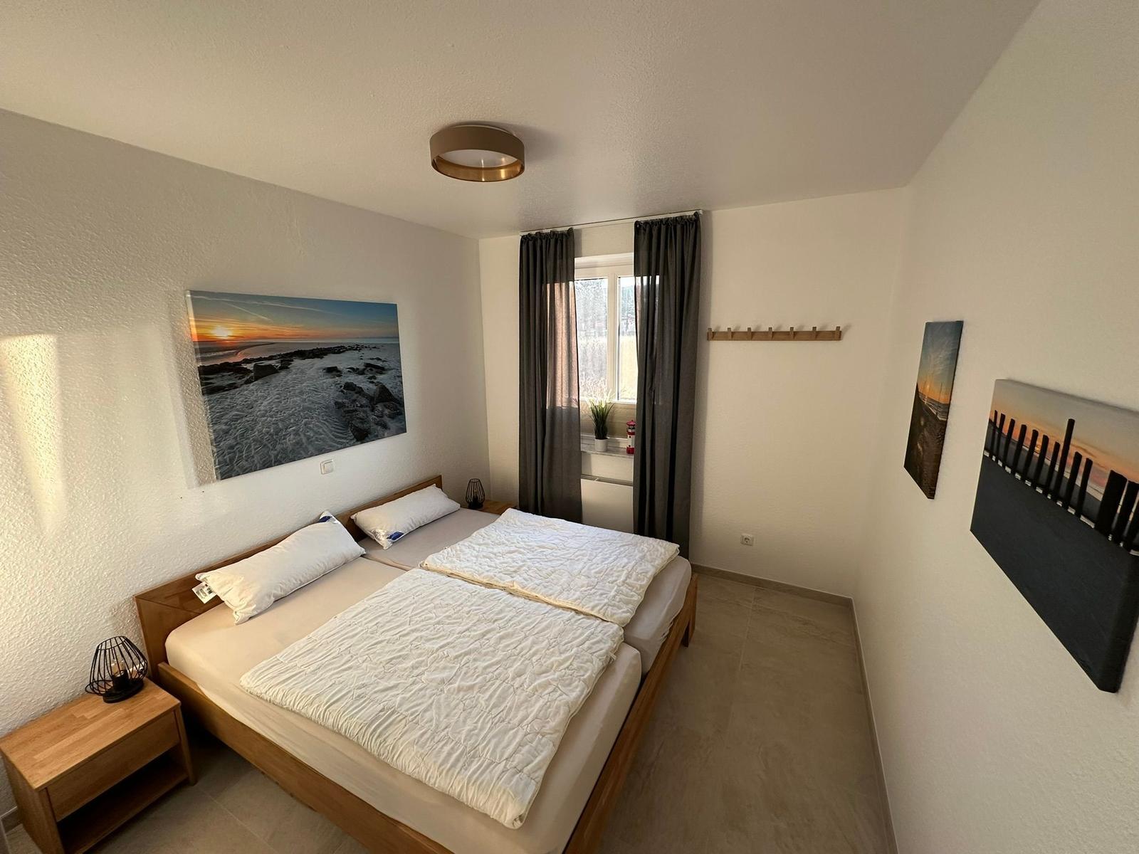 Schlafzimmer mit Doppelbett, Fenster und Wandbildern.