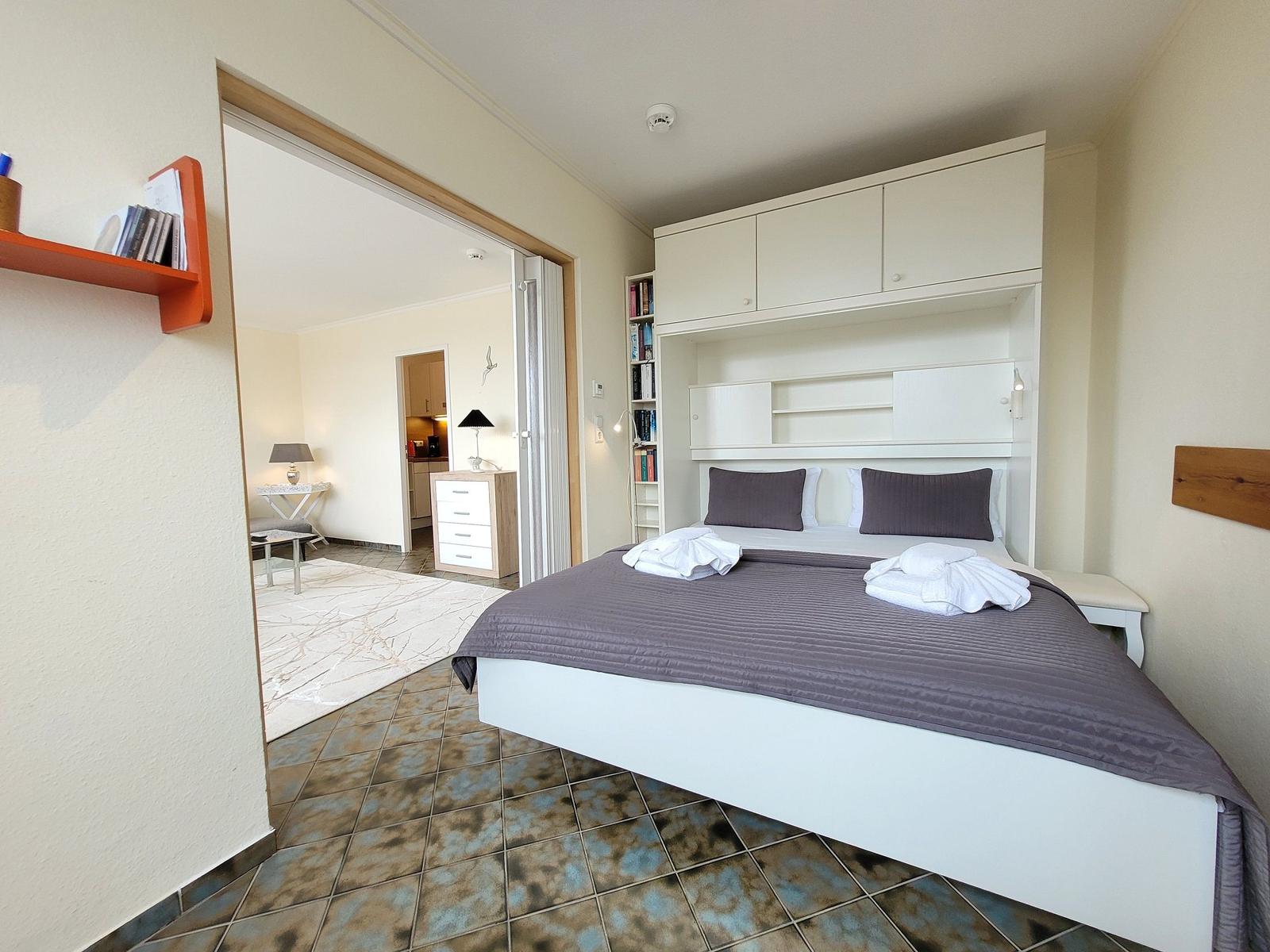 Schlafzimmer mit Bett, Schrank und Sicht auf Wohnbereich.