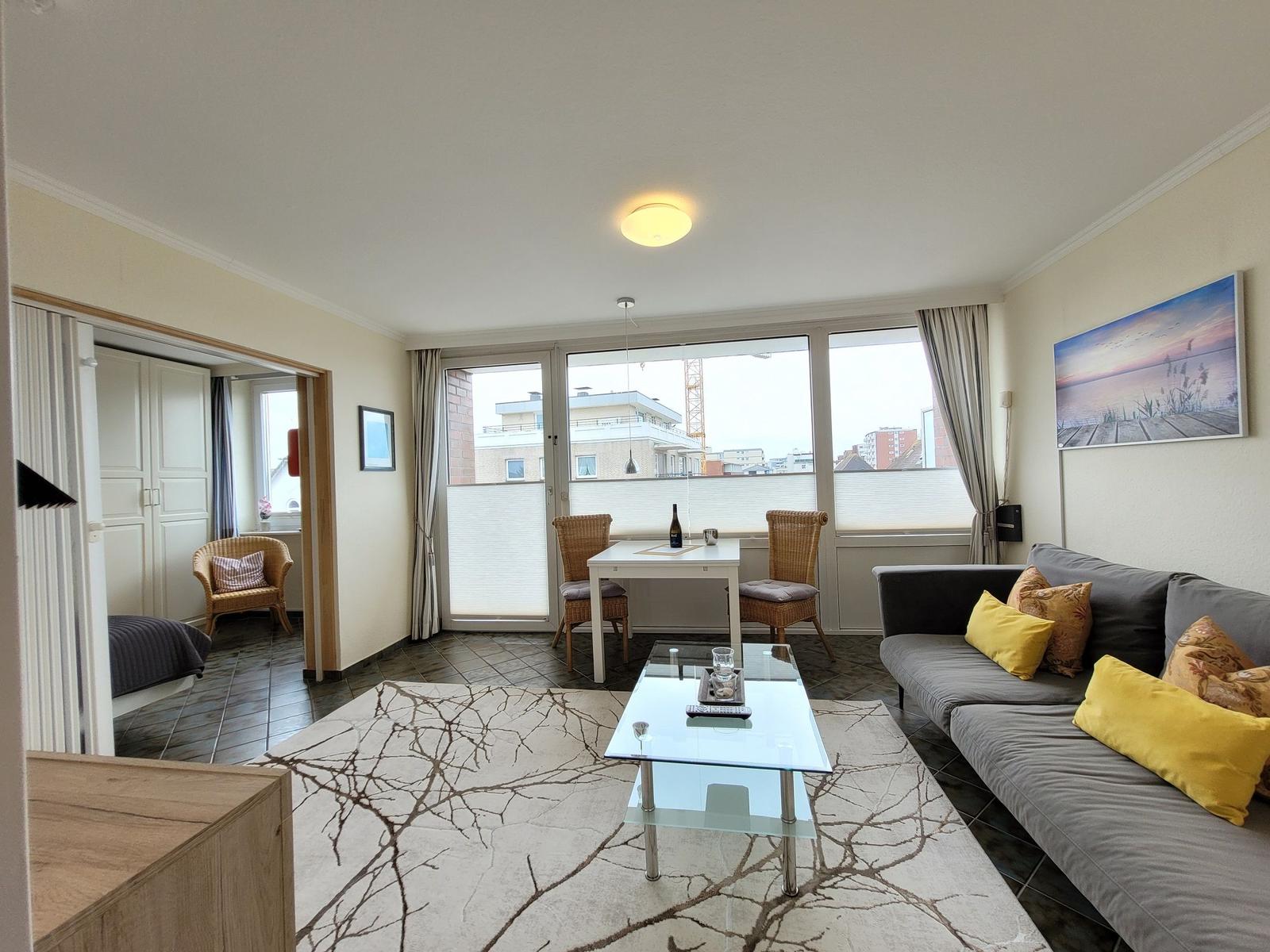 Wohnbereich mit Sofa, Esstisch und Blick auf Balkon.