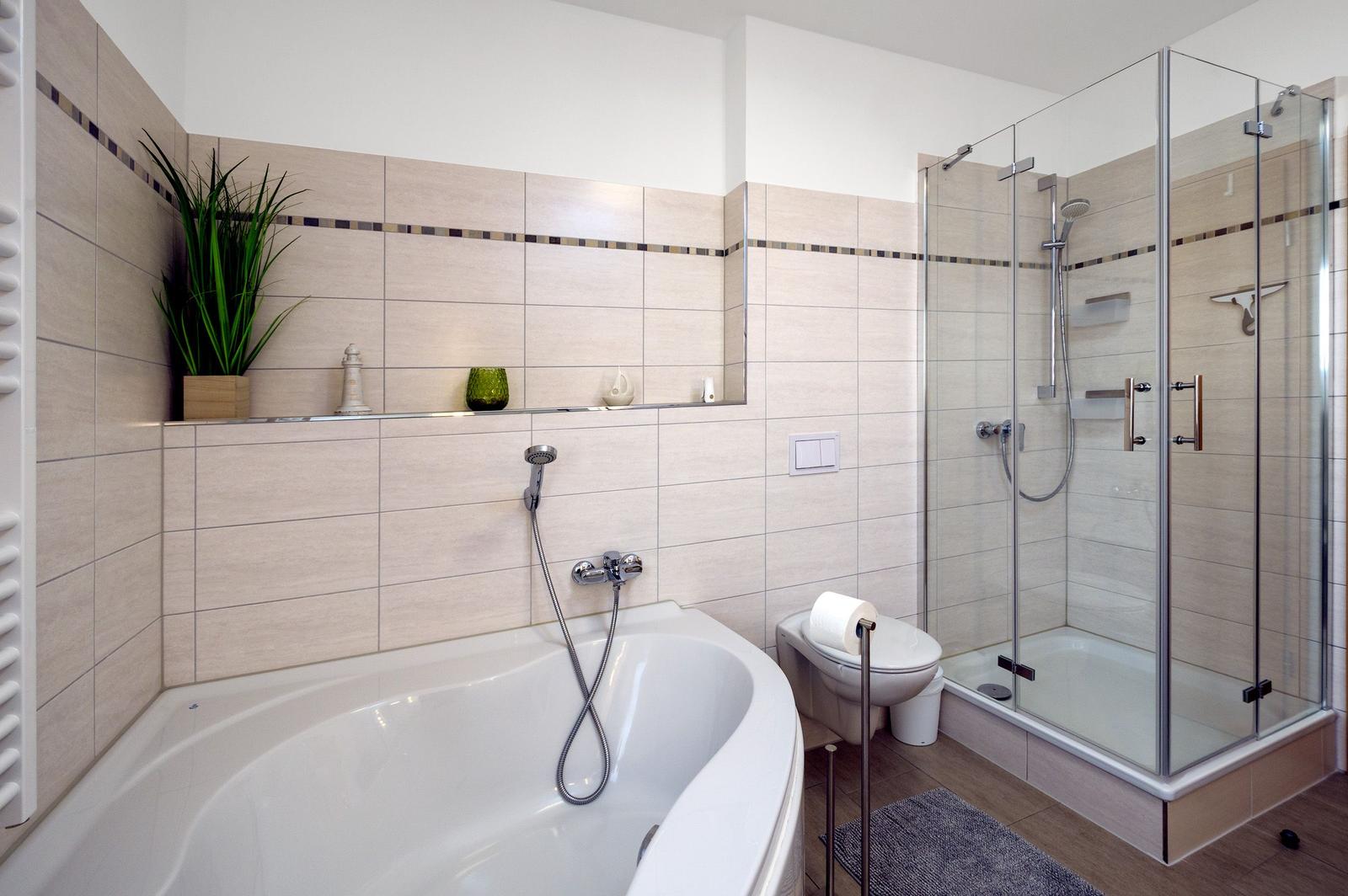 Badezimmer mit Badewanne, Dusche und Toilette. Wandfliesen mit dekorativer Strebe.
