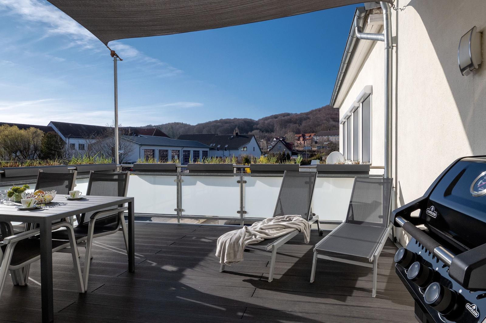 Terrasse mit Liegestühlen, Tisch, Grill und Blick auf die Berge.
