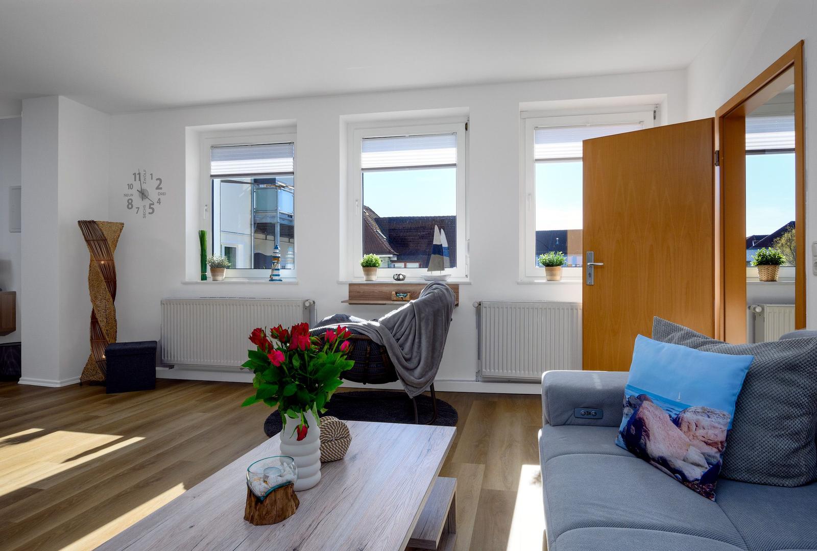 Wohnzimmer mit Sofa, Tisch, Fenstern und Tür.