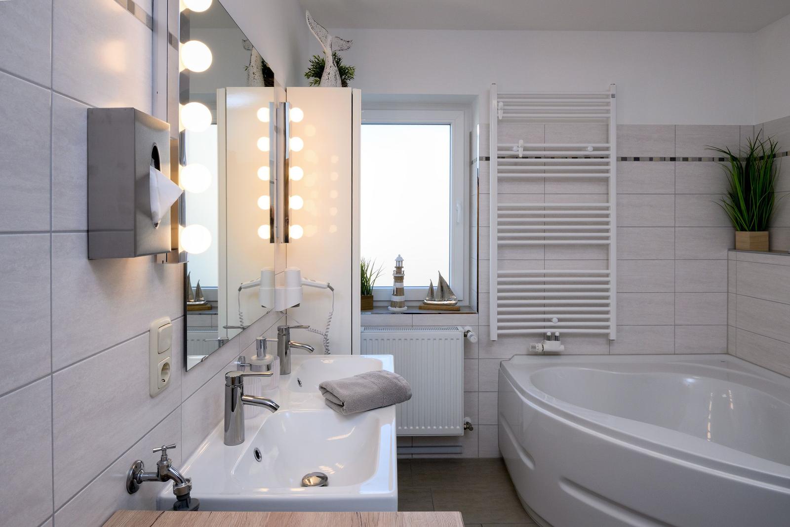 Badezimmer mit Dusche, Badewanne und beleuchtetem Spiegel.