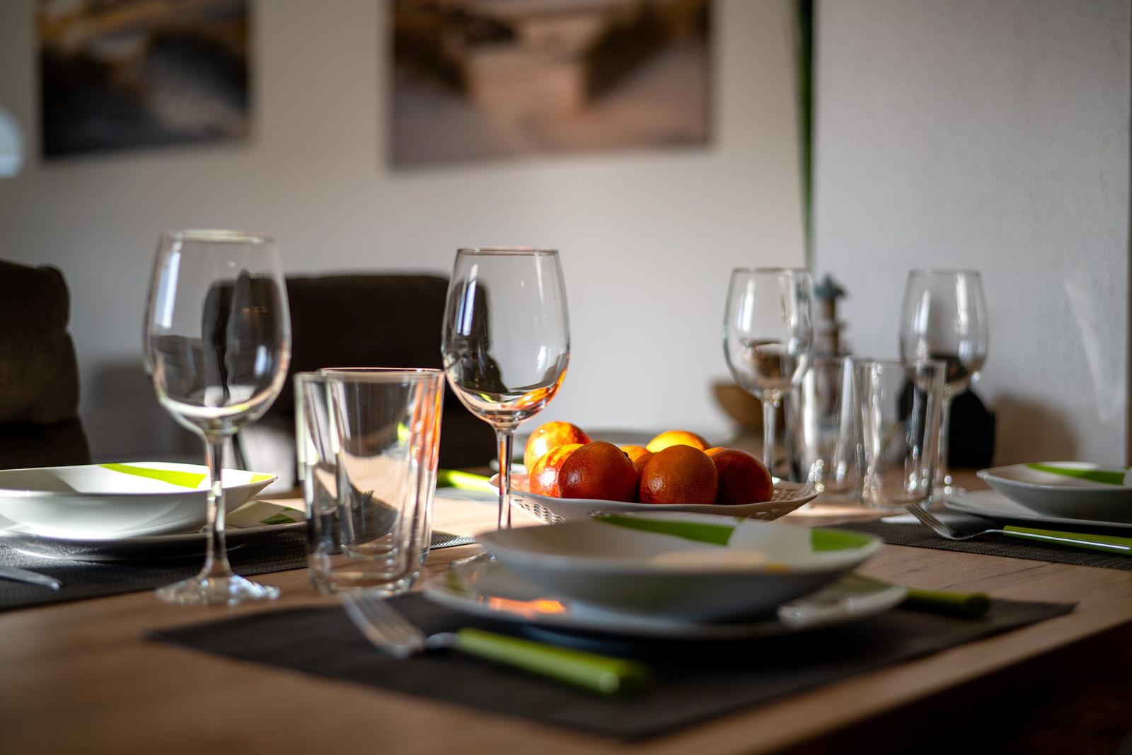 Tisch gedeckt mit Tellern, Gläsern und Obst. Hintergrund mit Wandbildern.