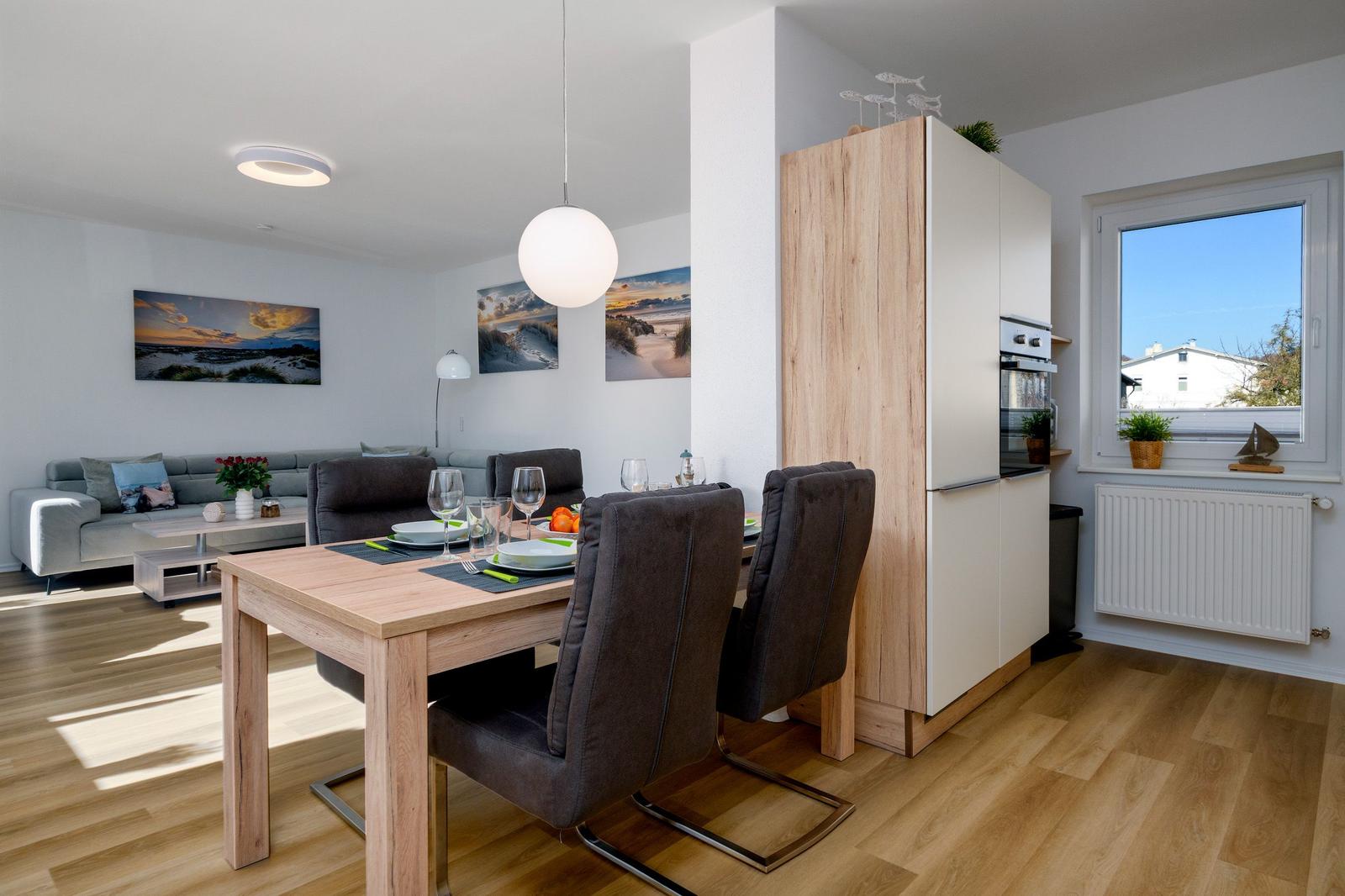 Esszimmer mit Tisch, Stühlen und Küchenzeile. Wohnbereich mit Sofa und Wandbildern.
