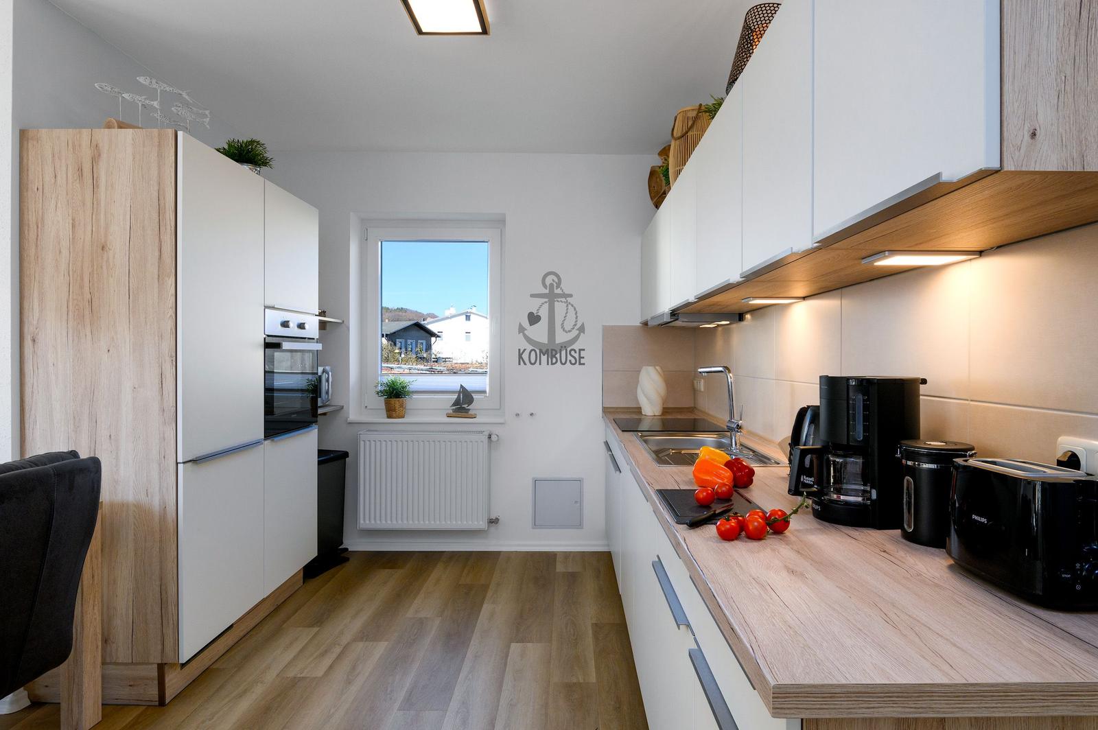 Küche mit Holzoberflächen, weißen Schränken und Fensterblick. Küchenzeile mit Spüle und Geräten.