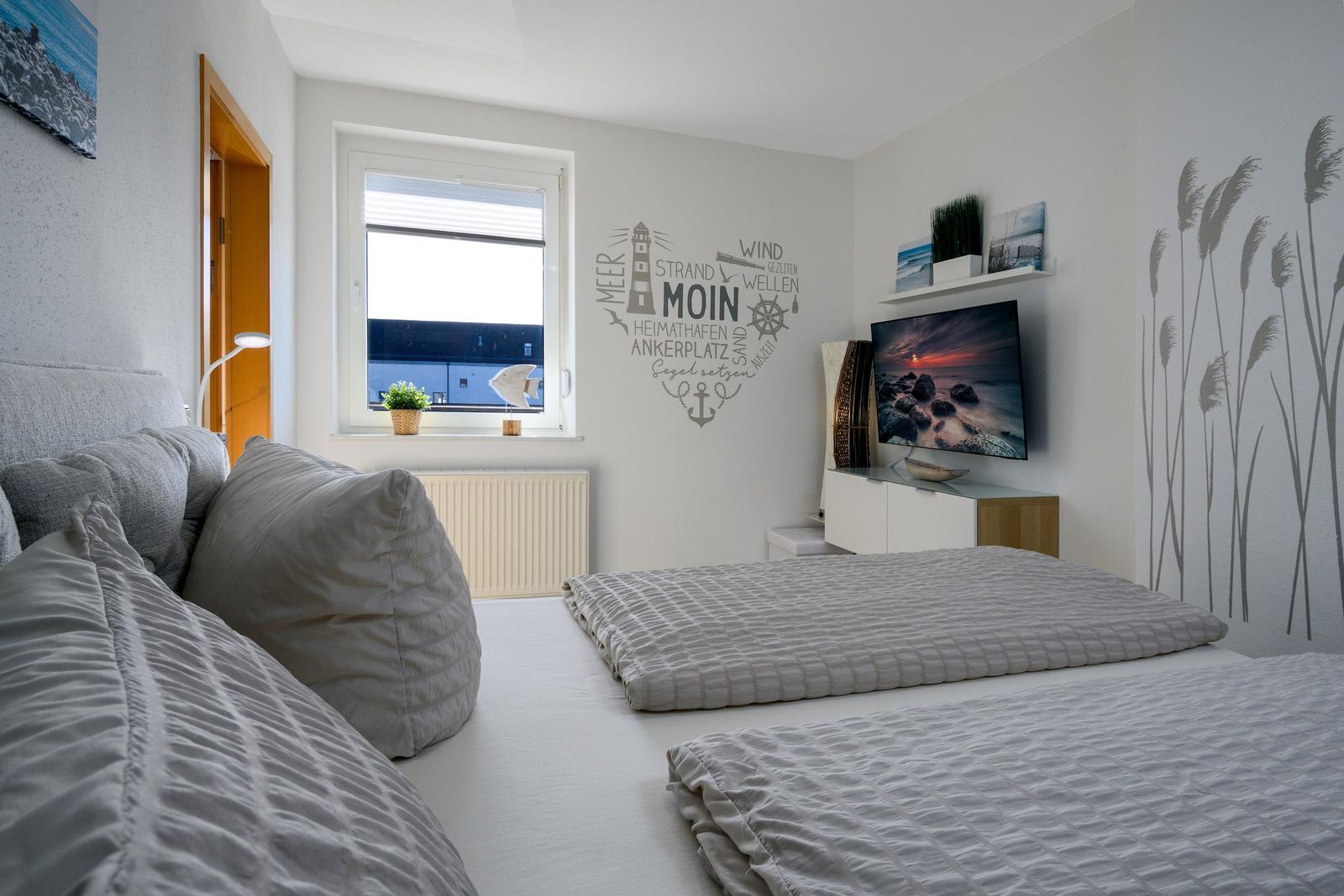 Schlafzimmer mit Bett, Fenster, Wanddekoration und Fernseher.