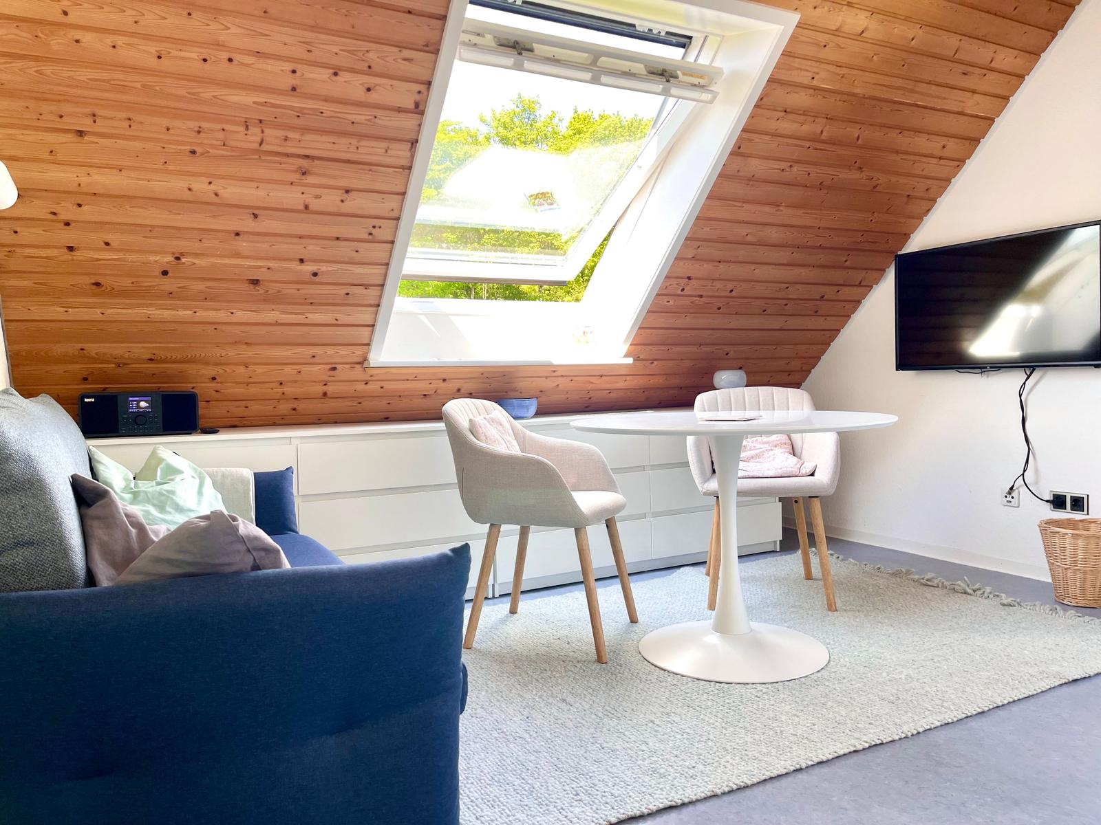 Wohnzimmer mit Dachfenster, Sofa, Esstisch und Fernseher an der Wand.
