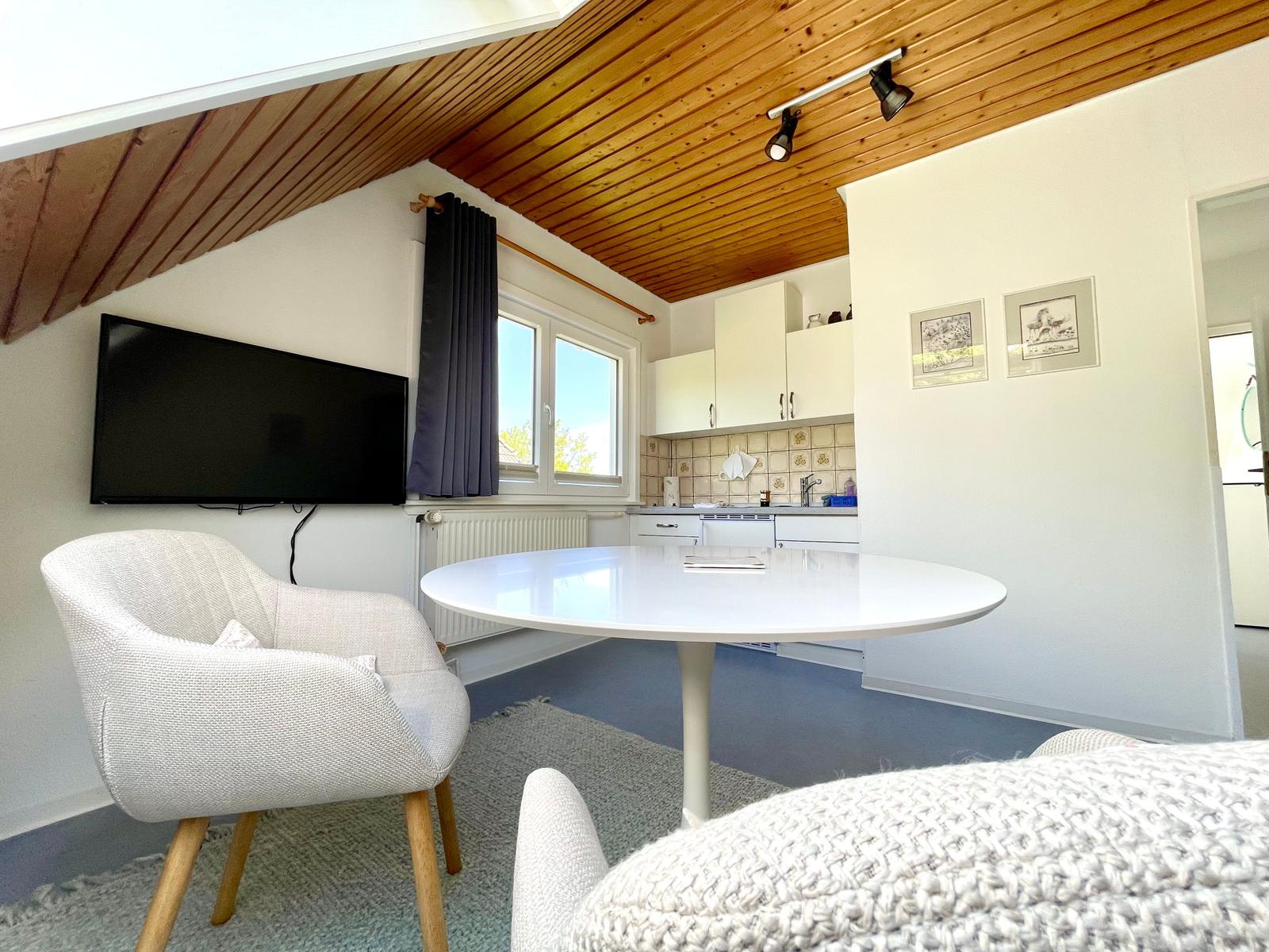 Wohn- und Küchenbereich mit runder Tisch, Fernseher und Holzdecke.