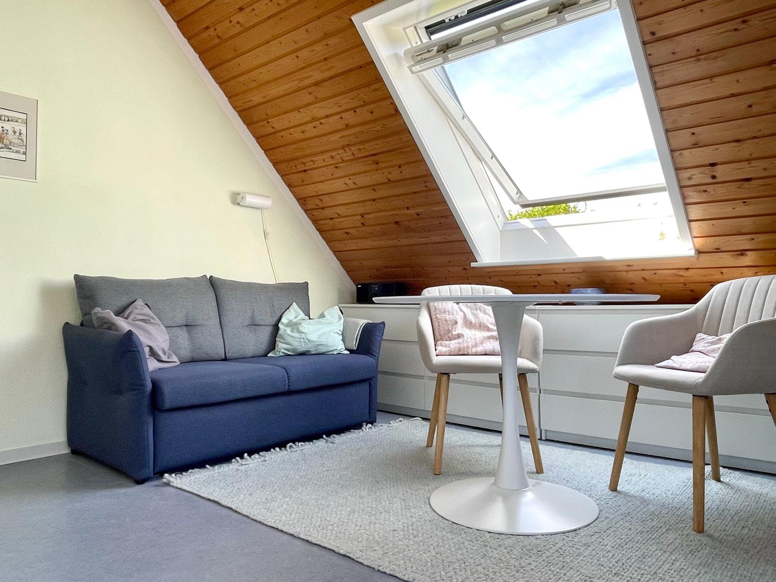 Ein Wohnraum mit Sofa, Tisch und Stühlen unter einer Dachschräge mit Fenster.