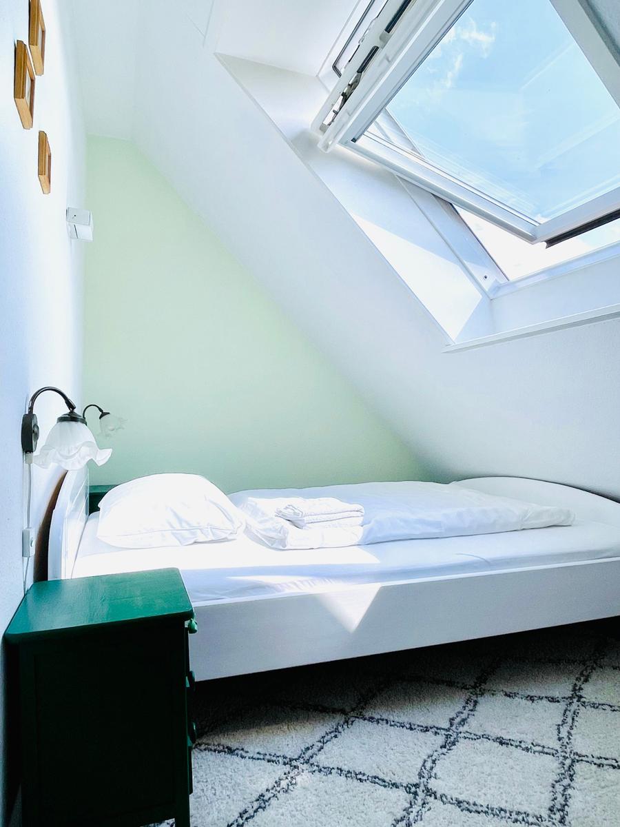 Schlafzimmer mit Dachschrägen, Fenster und Bett mit weißer Bettwäsche.