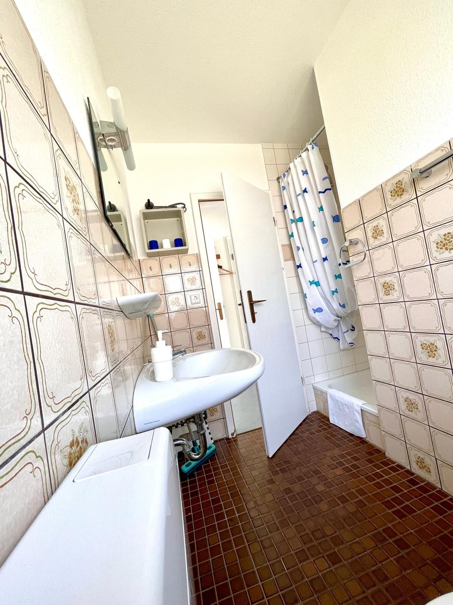 Badezimmer mit Dusche, Waschbecken und Toilette. Fliesen an Wänden und Boden.