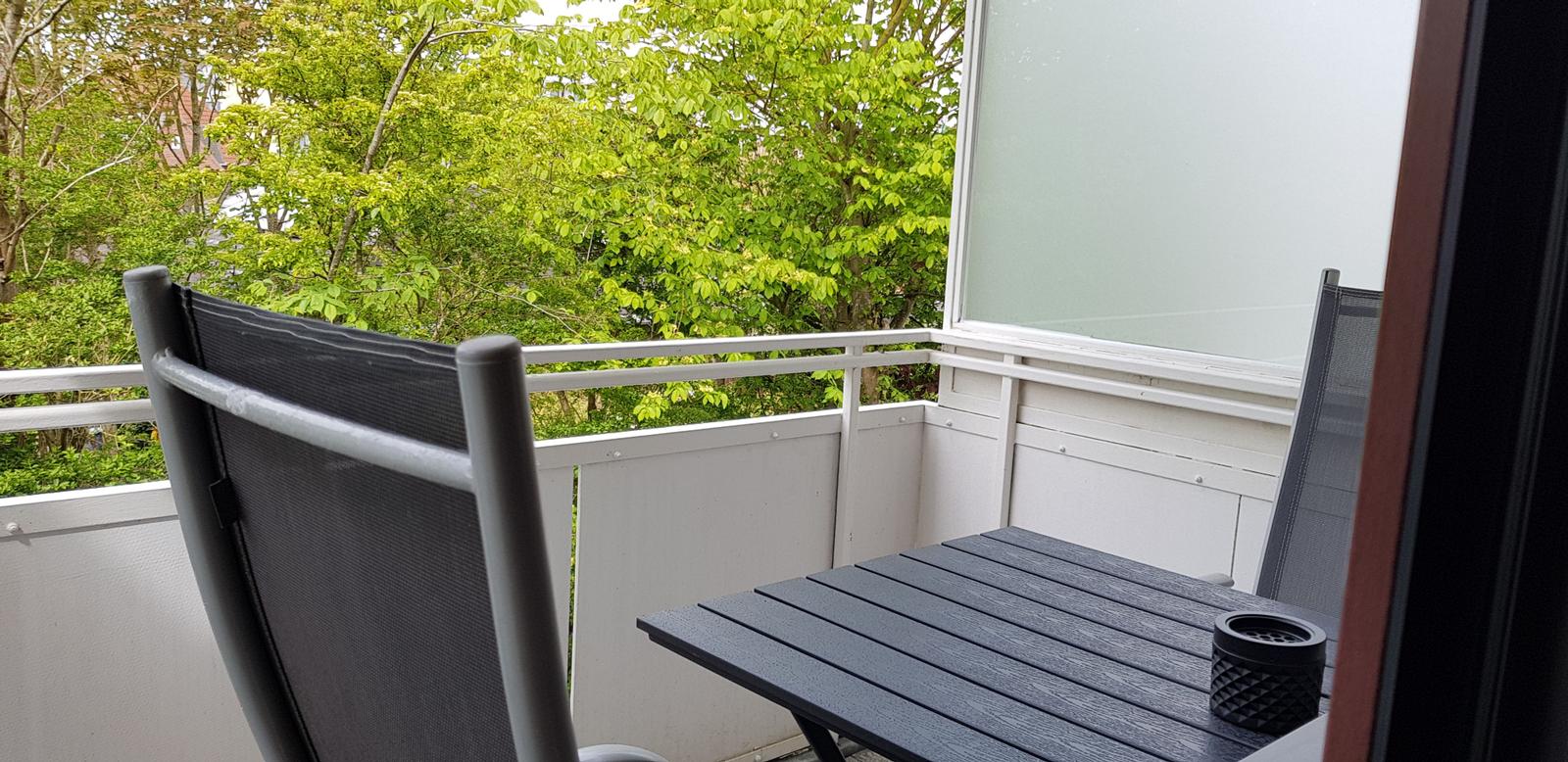 Terrasse mit Tisch und Stühlen. Blick auf grüne Bäume.