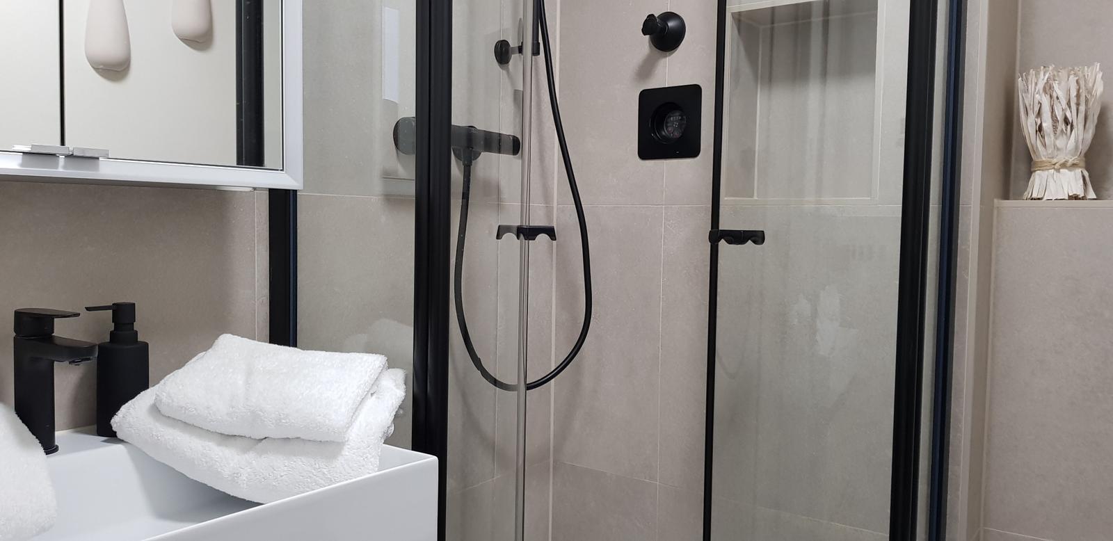 Dusche mit Glaswand, weiße Handtücher und schwarze Armaturen.