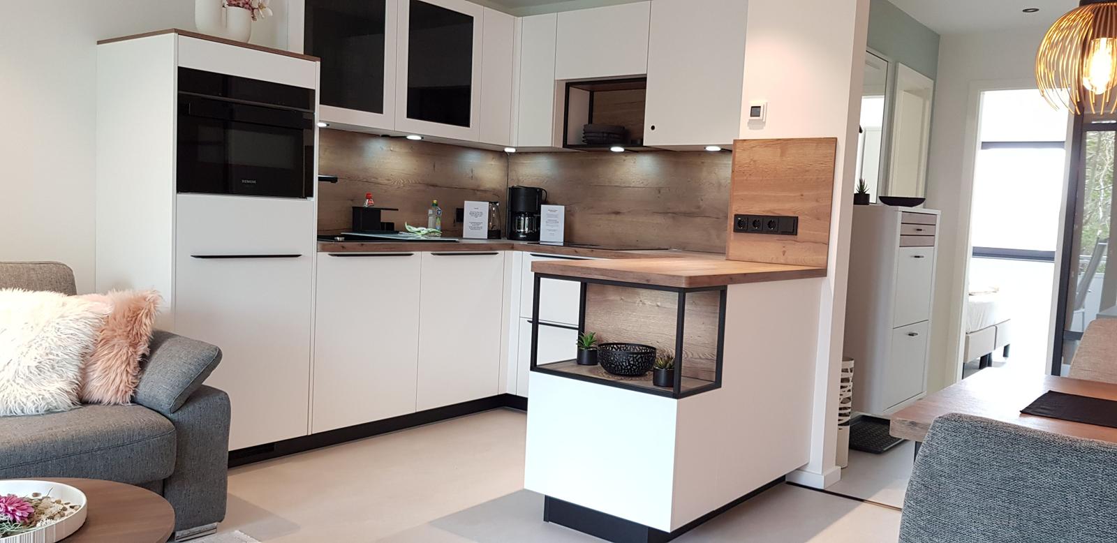 Moderne Küche mit Arbeitsplatte, Schränken und integriertem Ofen. Wohnbereich mit Sofa und Essbereich sichtbar.