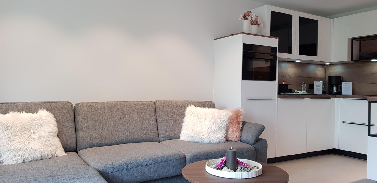 Ein grauer Sofa mit flauschigen Kissen und eine moderne Küche im Hintergrund.