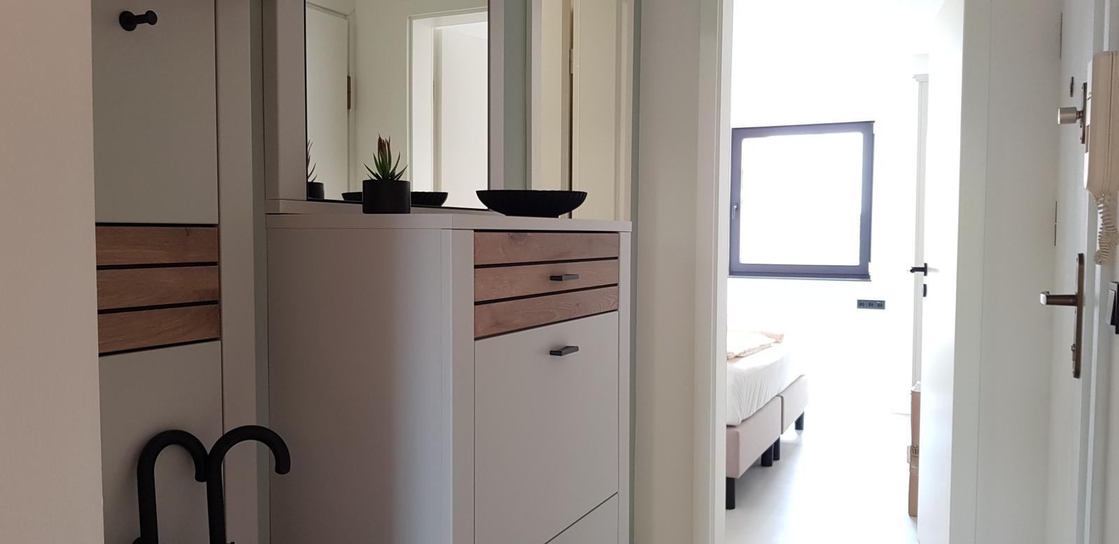 Schlafzimmer mit Bett und Fenster. Flur mit Schrank, Spiegel und Pflanze.