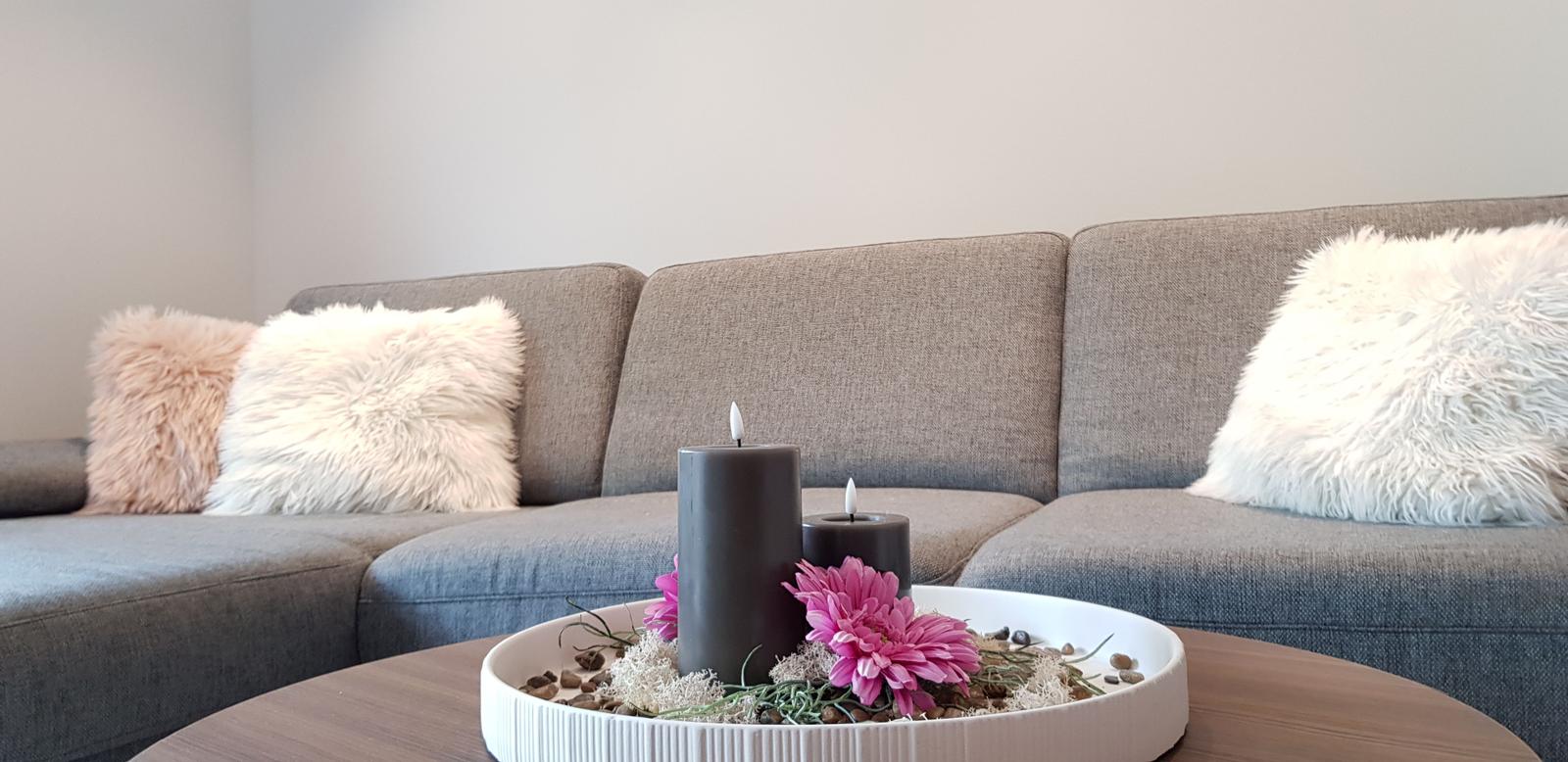 Grauer Sofa mit Fellkissen und Tisch mit Kerzen und Blumen